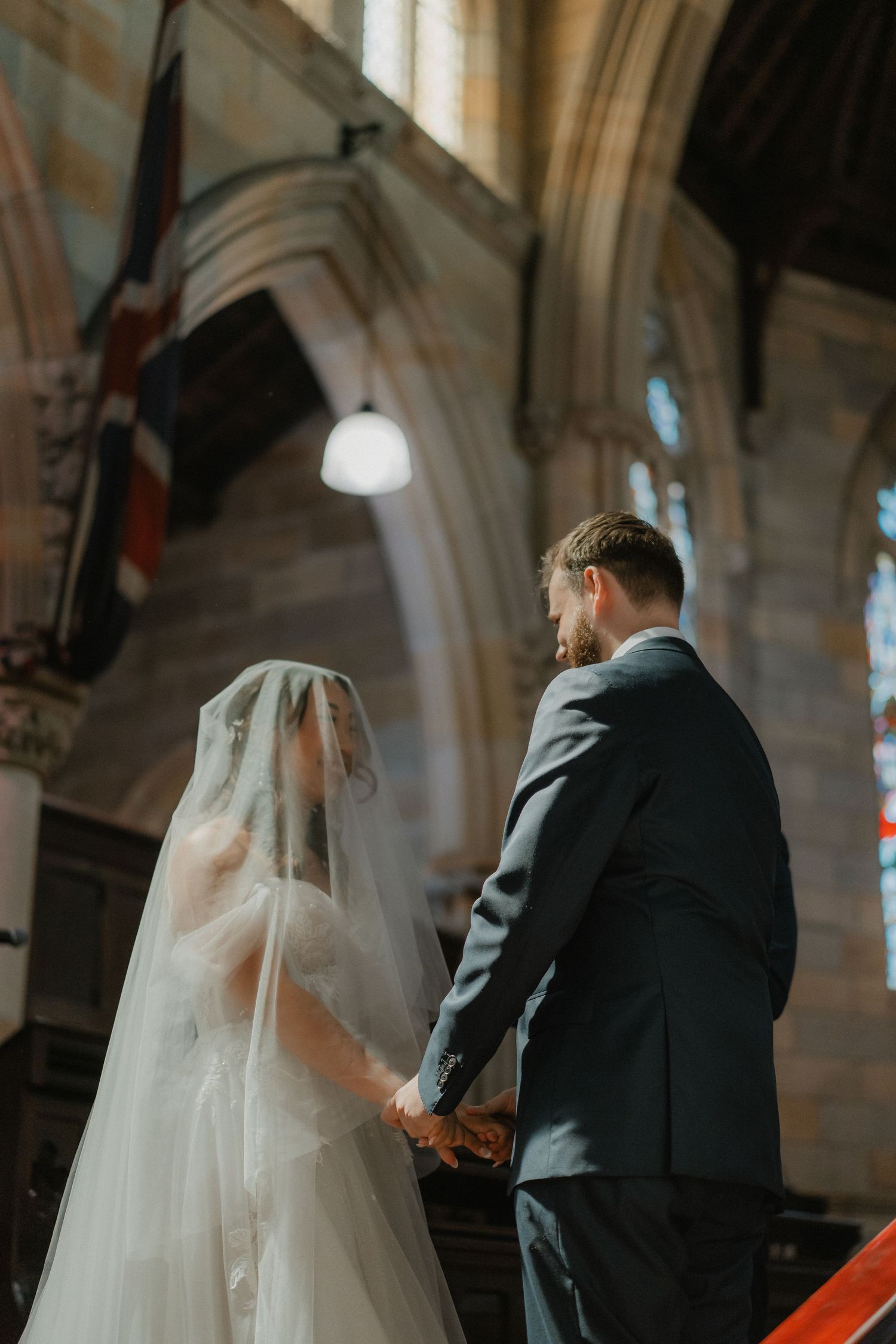 Ethereal church ceremony captured from behind with gothic arches and soft natural light filtering through windows.