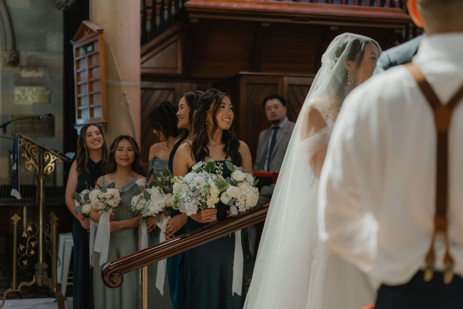 Wedding ceremony in a historic church with bridesmaids watching from wooden pews.