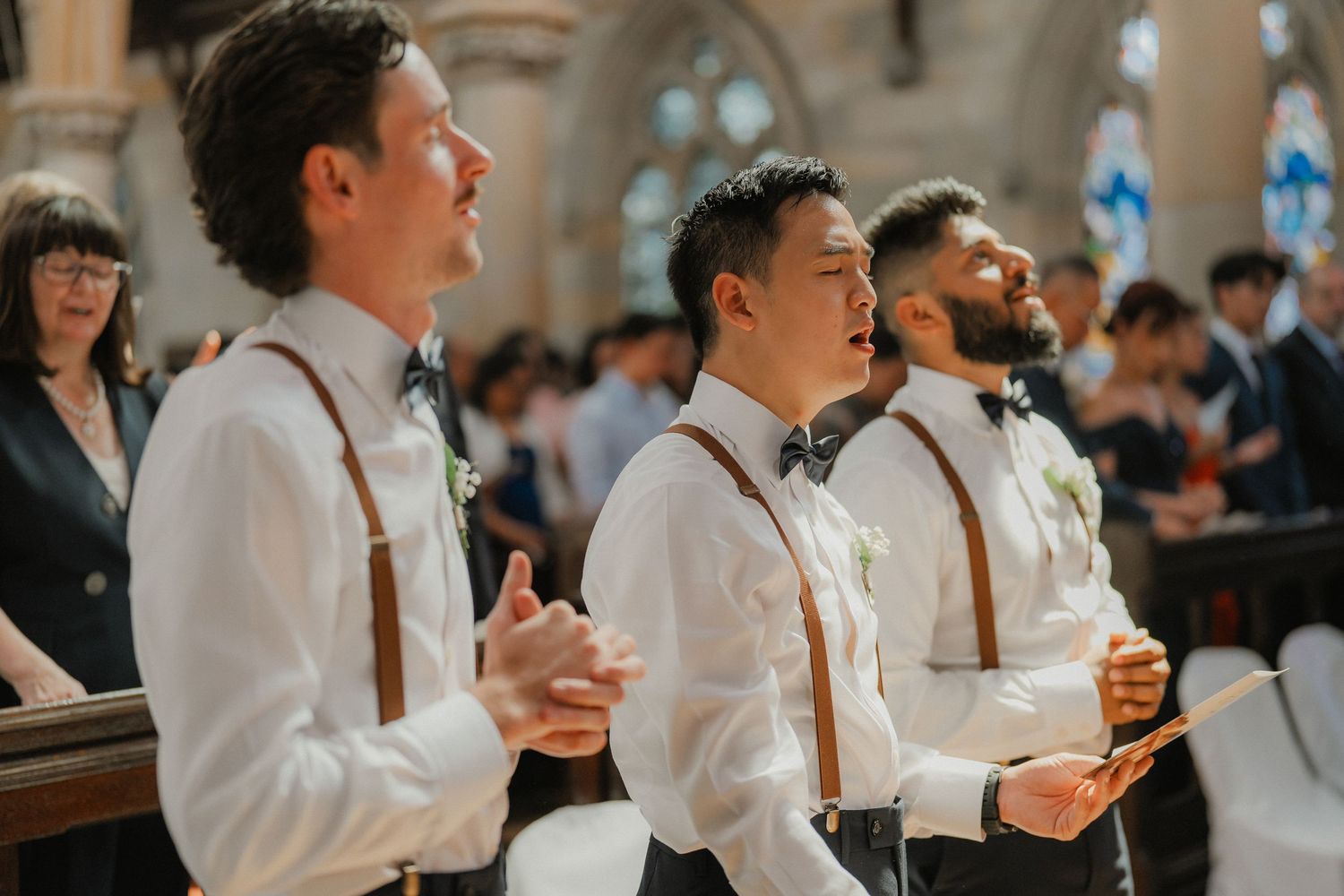 Groomsmen in white shirts and bowties sing during a church wedding ceremony.