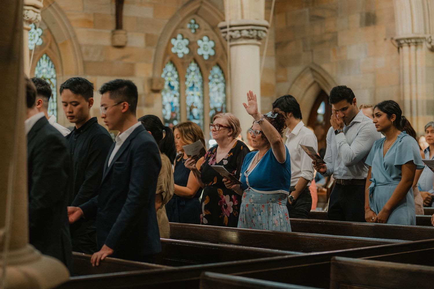 Wedding attendees gather in church pews beneath gothic arches and stained glass windows.