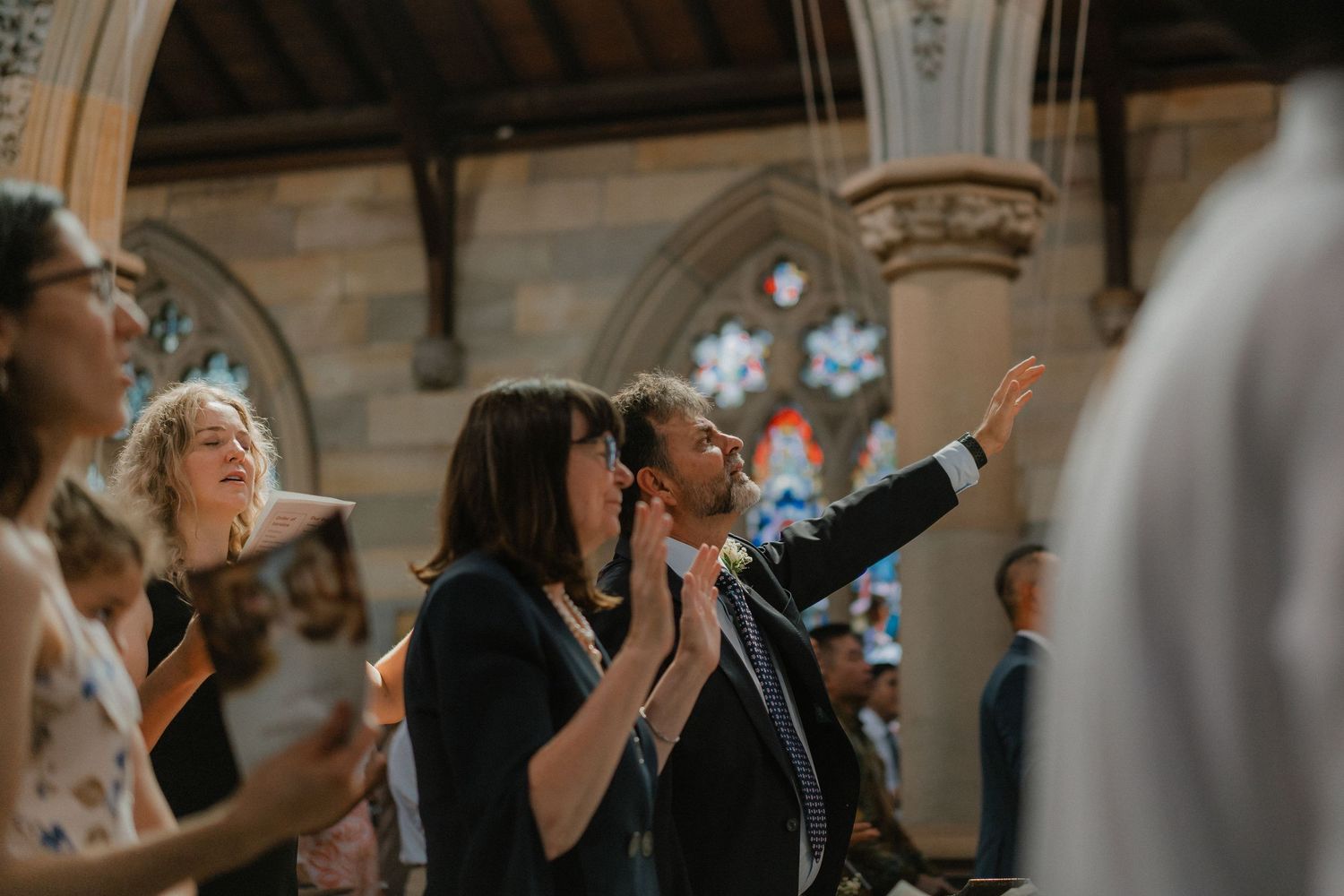 Congregation members worship together during a church service with historic architecture and stained glass windows.