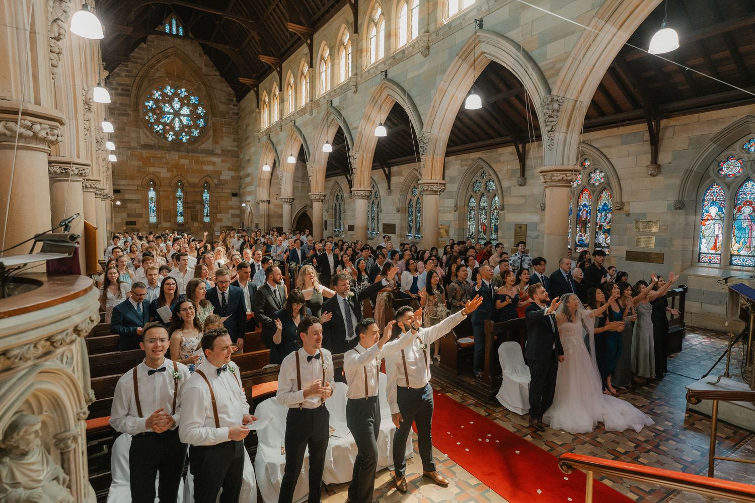 Large group gathered in a traditional church for a wedding ceremony with gothic architecture and arched ceilings.