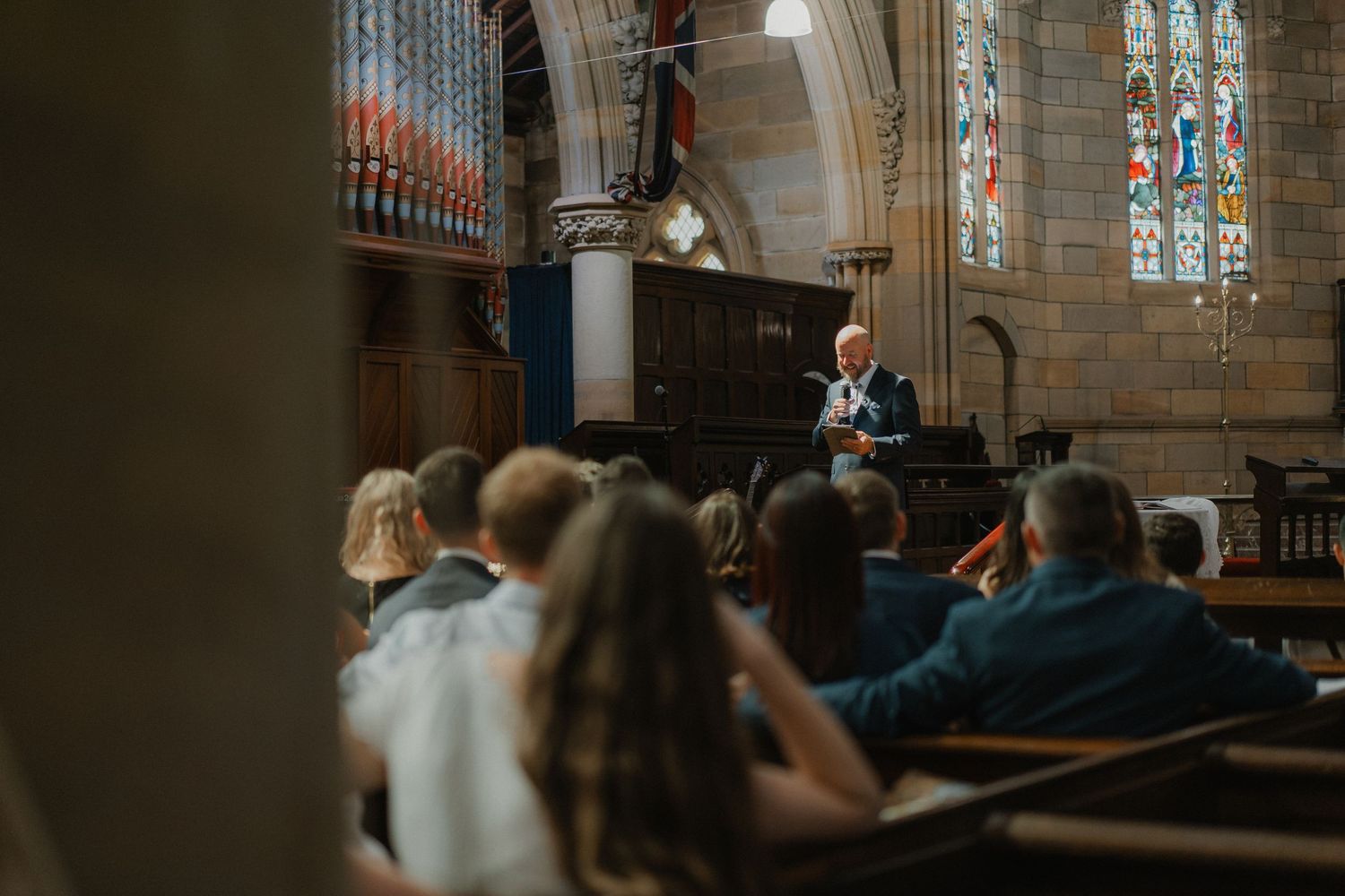 Interior view of a traditional church sanctuary with wooden pews and stained glass windows during a service.