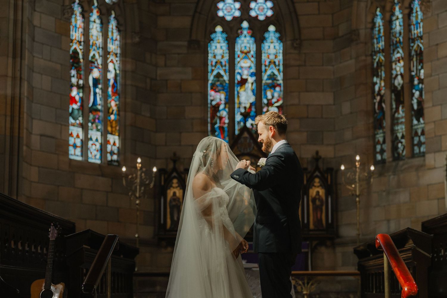 A couple shares an intimate moment during their wedding ceremony under stunning stained glass windows in a gothic church.