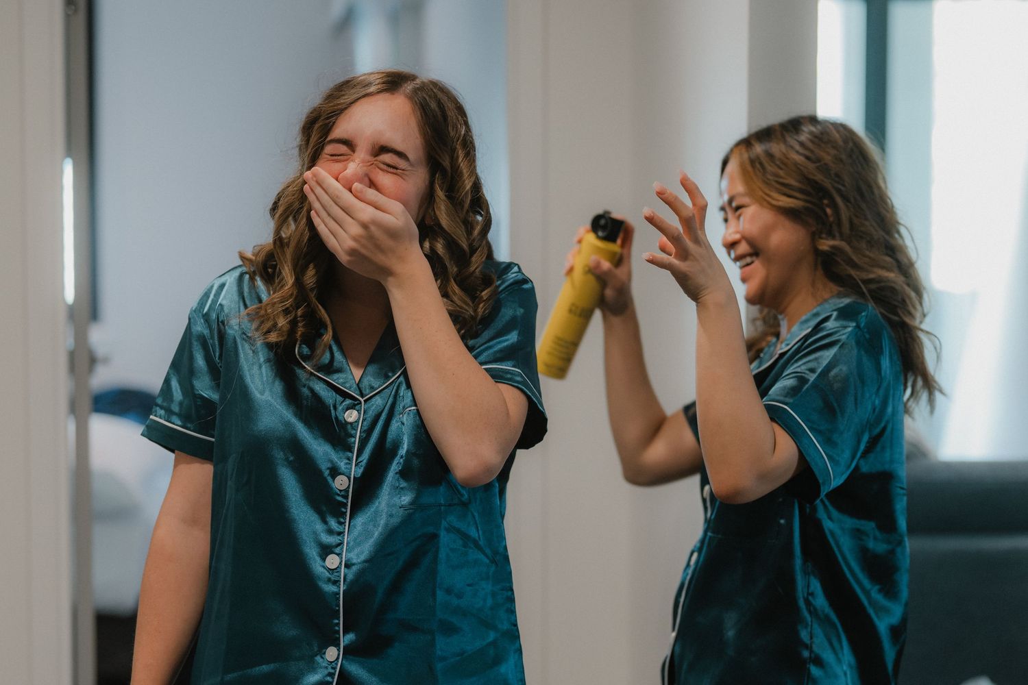 Bridesmaids in teal silk robes share an excited moment during wedding preparations.