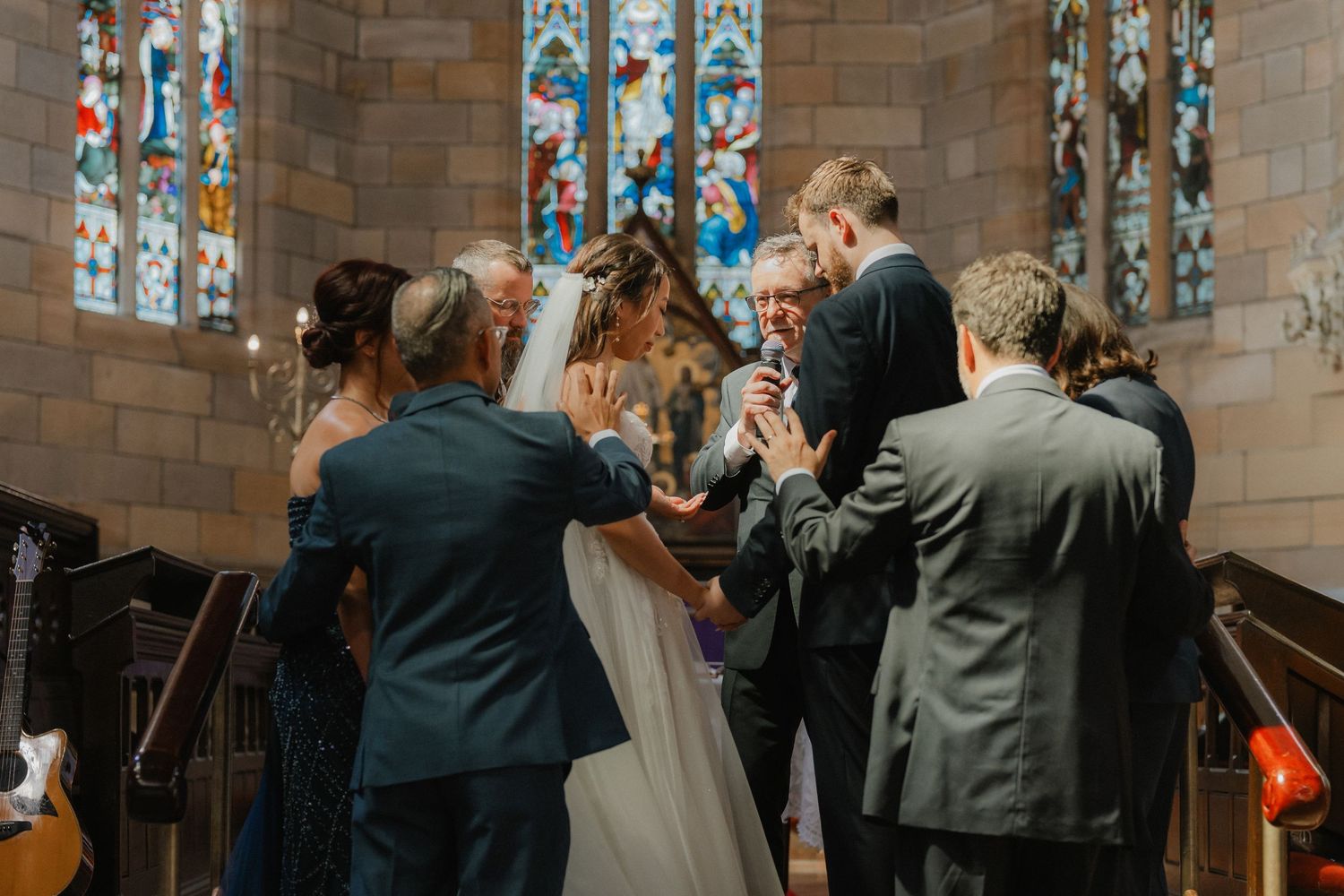 Wedding ceremony in a church with stained glass windows as guests gather around the couple.
