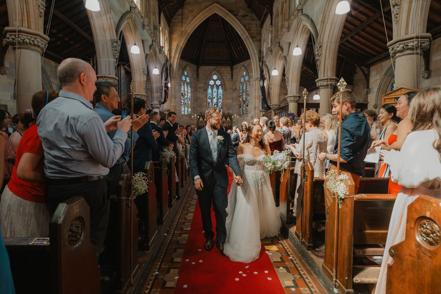 Guests line the church aisle during wedding ceremony in historic cathedral with gothic arches.
