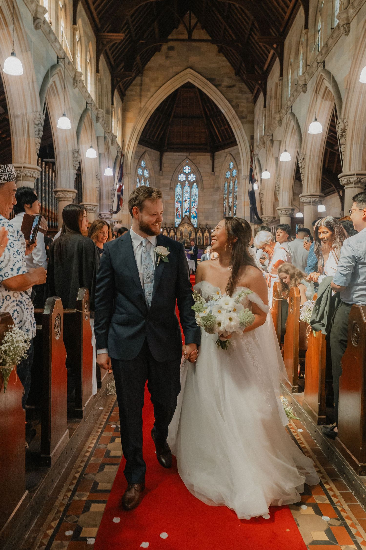 Wedding ceremony inside a gothic church with ornate stone columns and stained glass windows along the aisle.