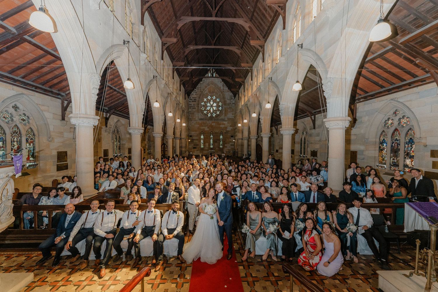 Wide view of wedding ceremony in historic church filled with guests on wooden pews.