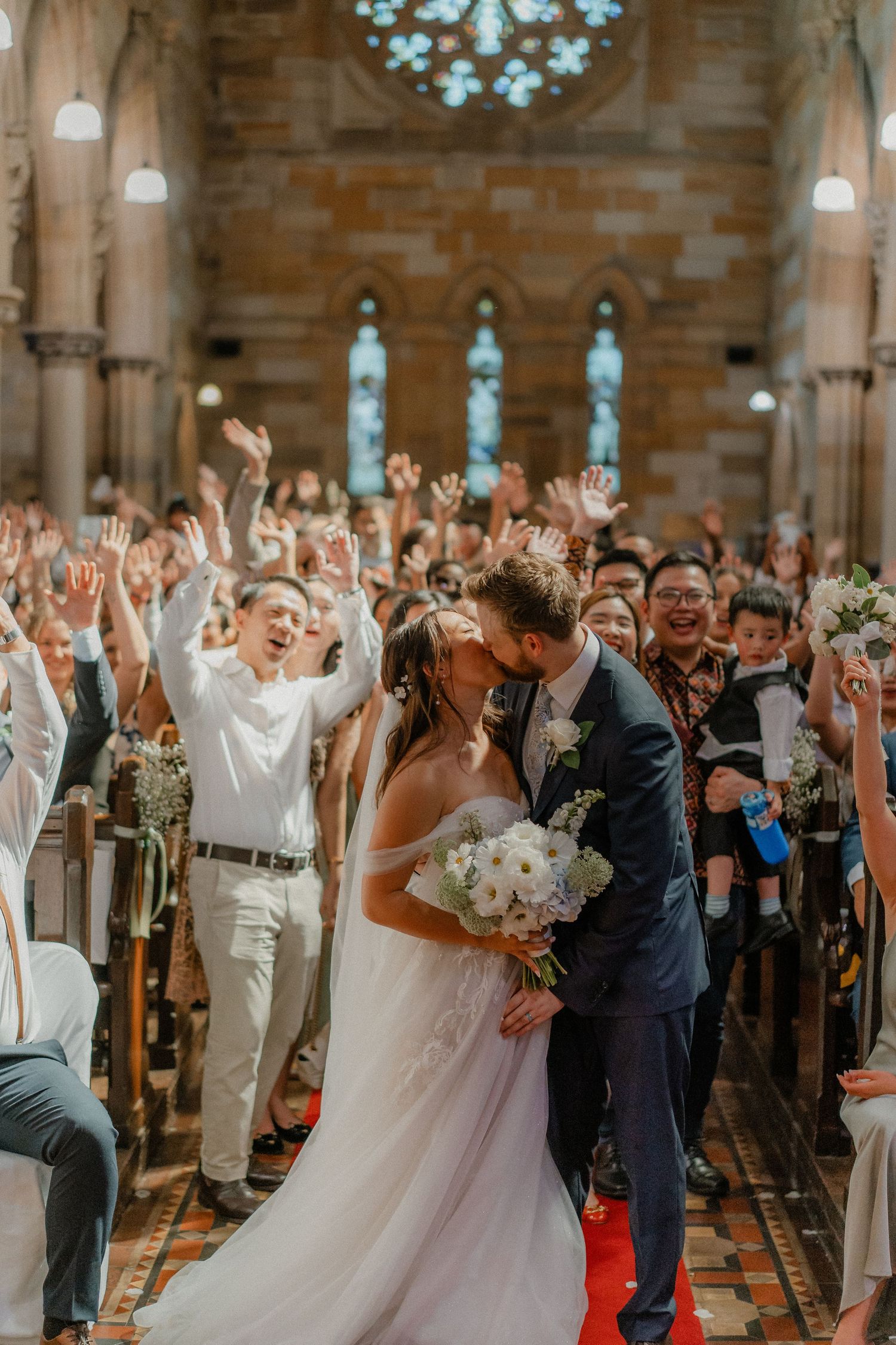 Celebration erupts inside historic church as wedding guests cheer and raise hands in joy.