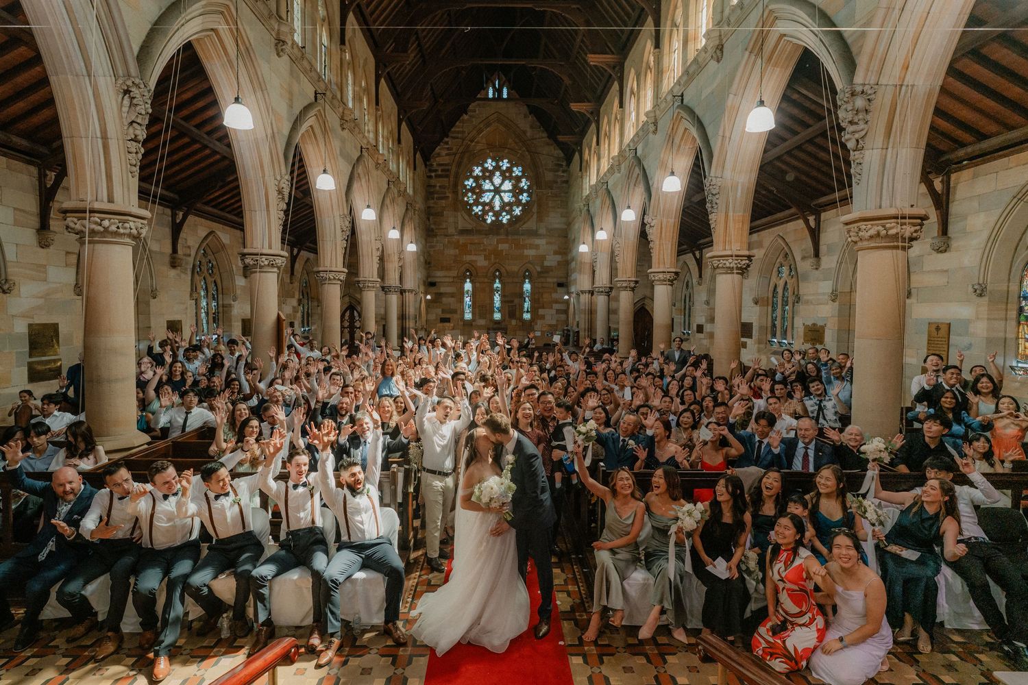 Wide angle shot of a church wedding ceremony with guests filling the pews under vaulted gothic architecture.