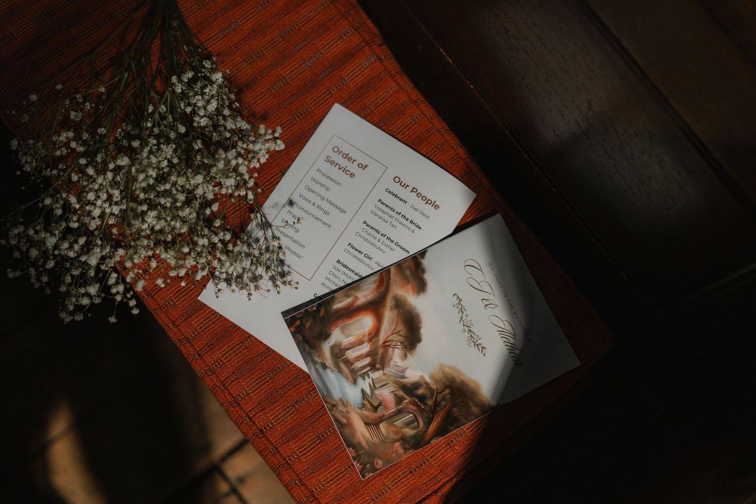 Wedding details including invitation and baby's breath flowers on a wooden surface in moody lighting.