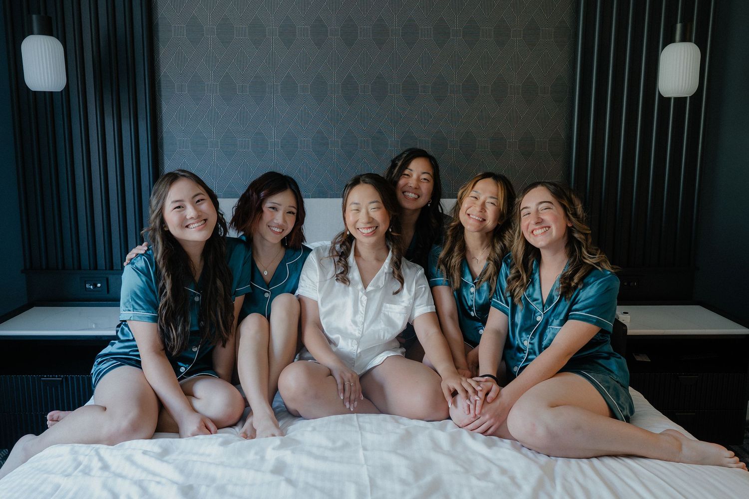 Group in matching blue robes and white dress sitting together on bed during morning celebration.