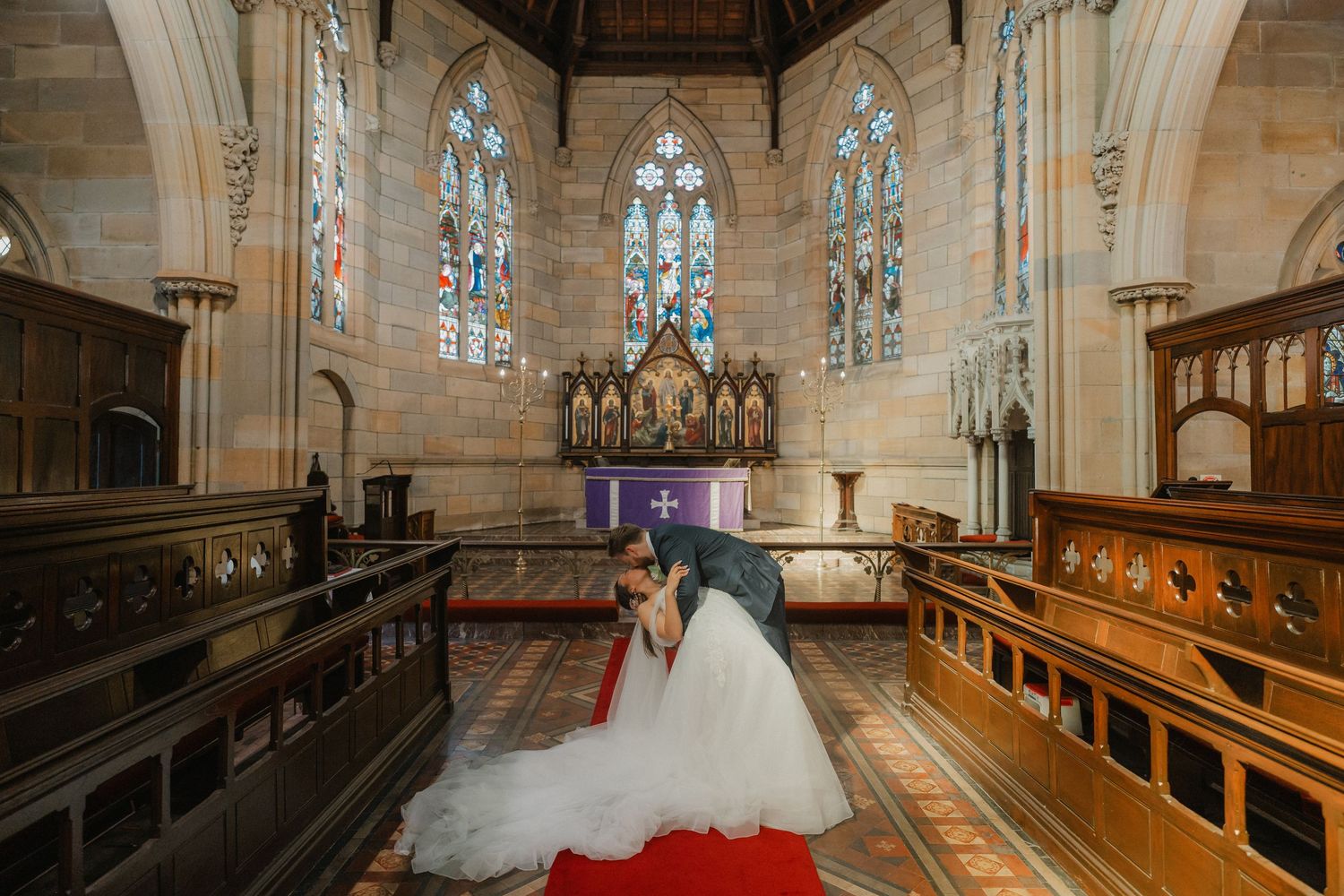 Dramatic wide shot of a church interior with stained glass windows and wooden pews on a wedding day.