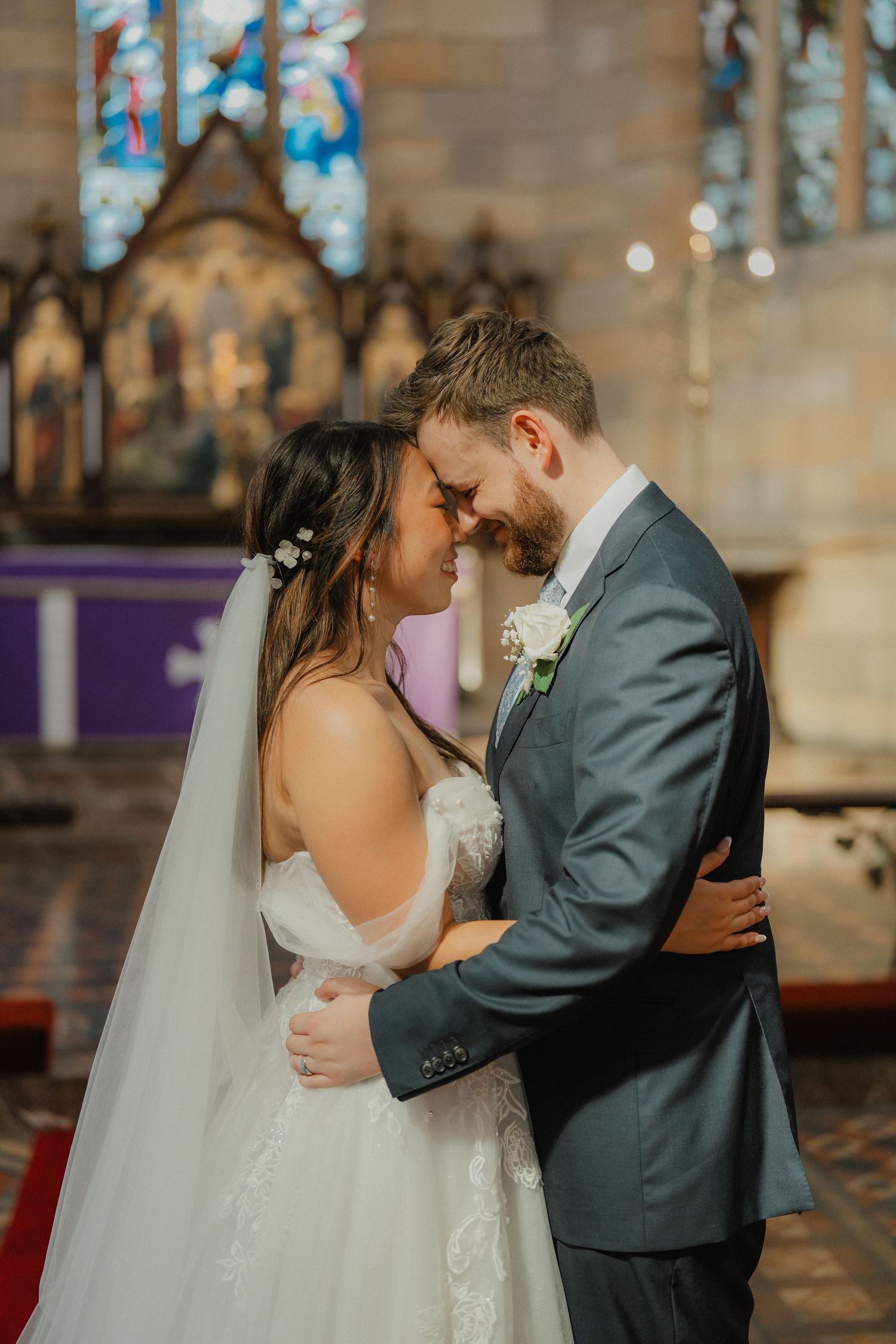 Intimate wedding ceremony moment in a historic stone church with stained glass windows.