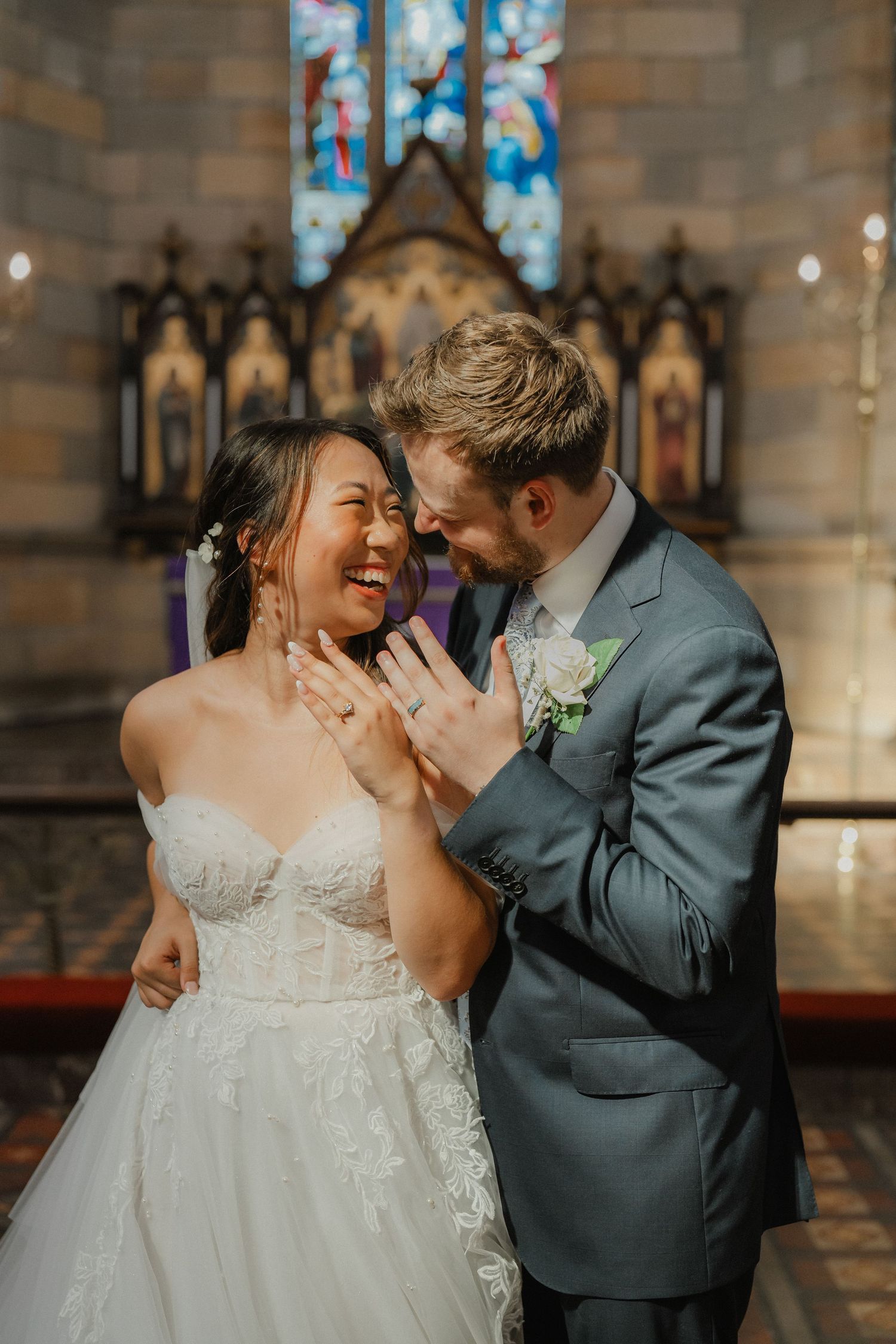 A joyful wedding moment captured in front of a gothic church altar with colorful stained glass windows.