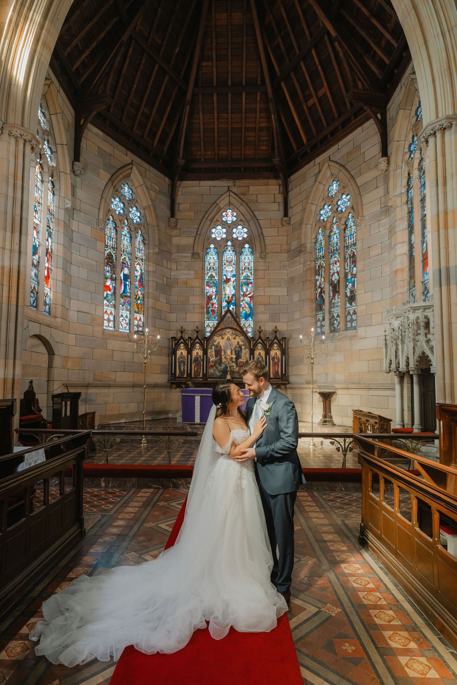 A couple shares an intimate moment in a historic church with stained glass windows and vaulted wooden ceiling.