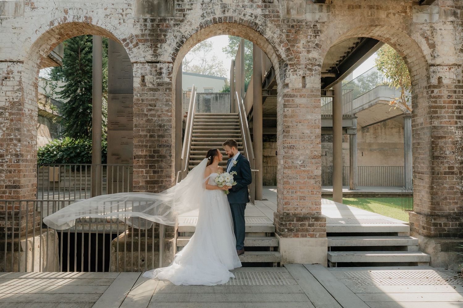 A romantic wedding portrait on stone steps framed by historic brick archways.