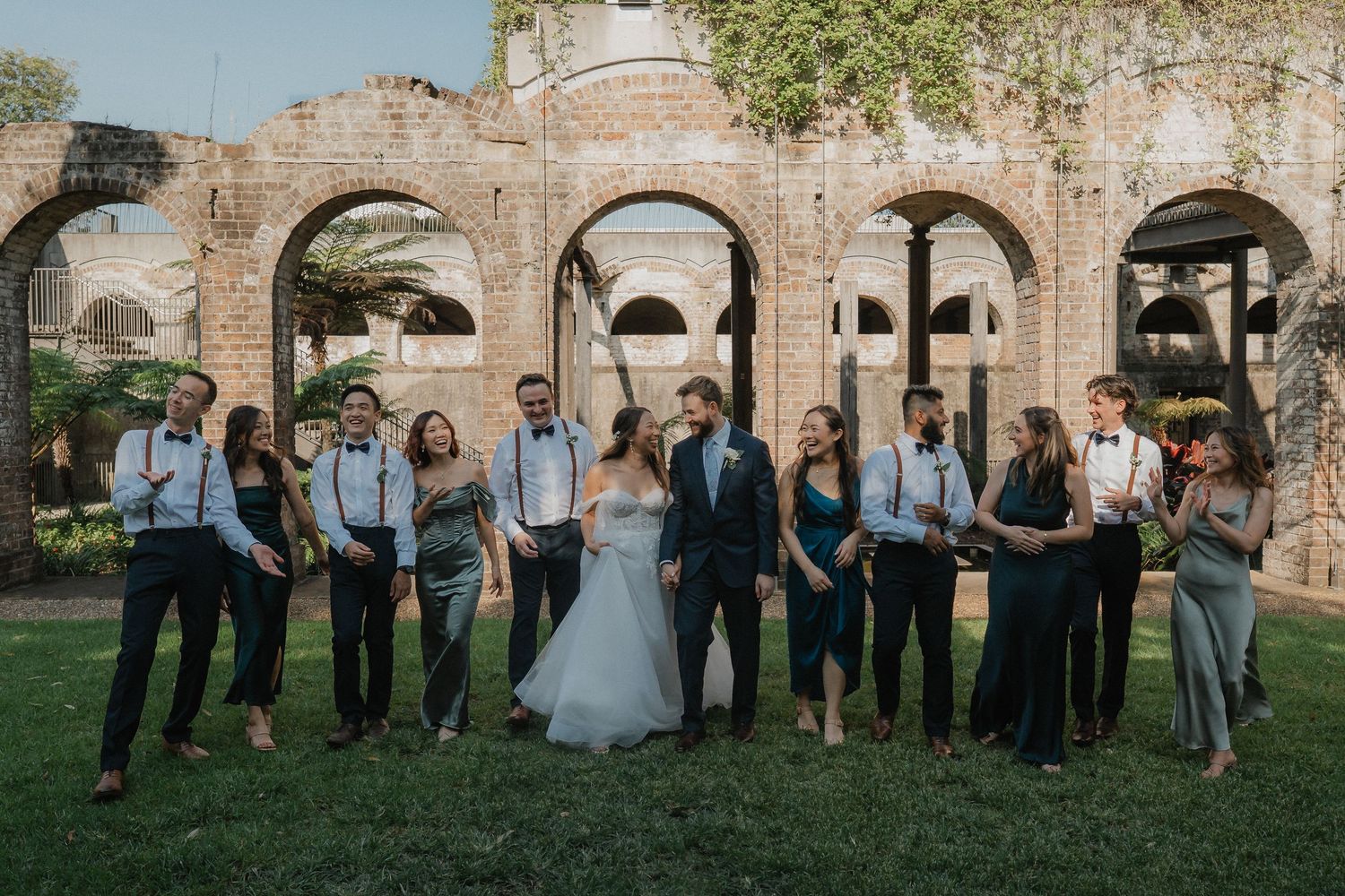 Wedding party poses in front of historic stone arches and architecture.