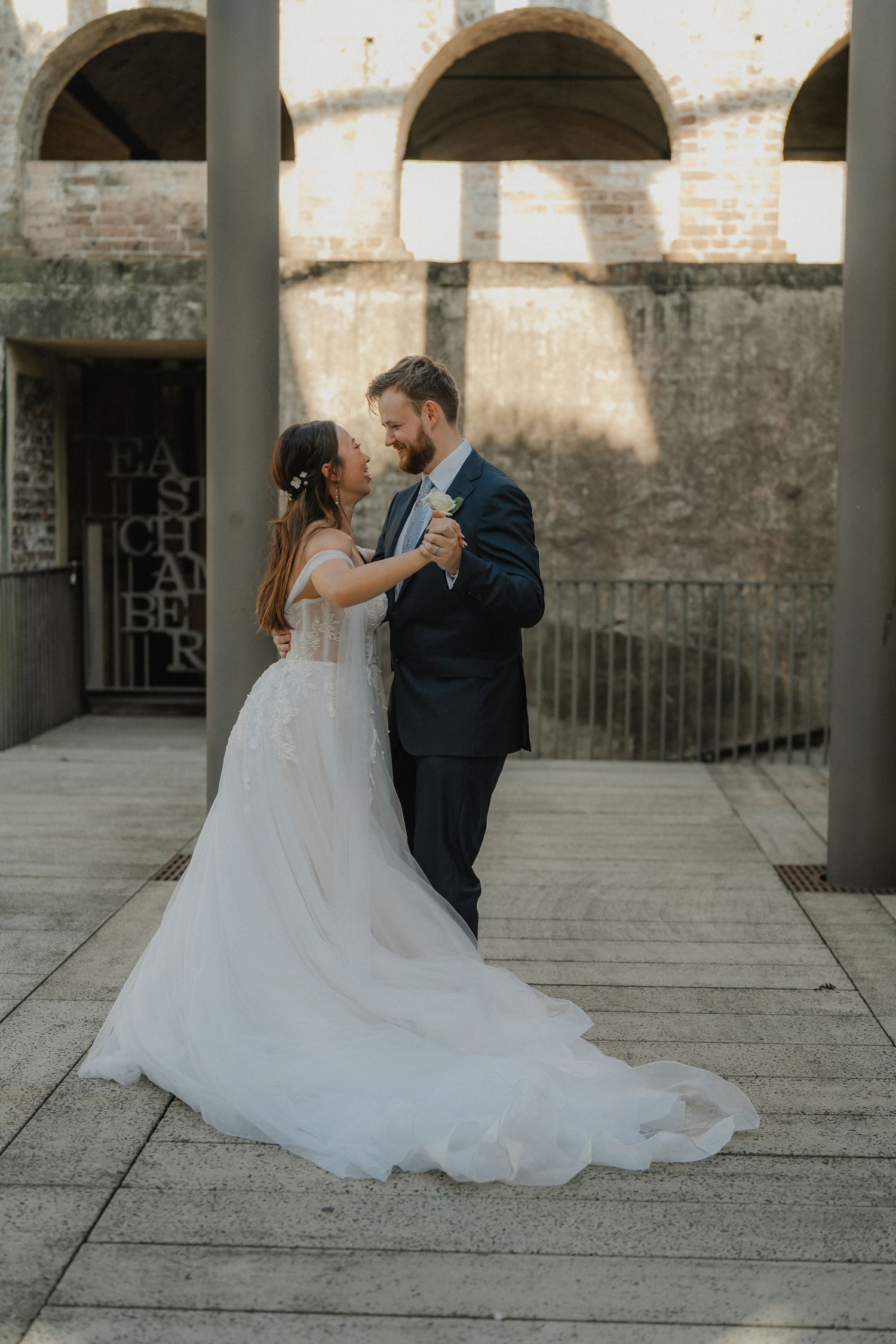 Elegant wedding couple shares an intimate dance moment under historic arched stone architecture.