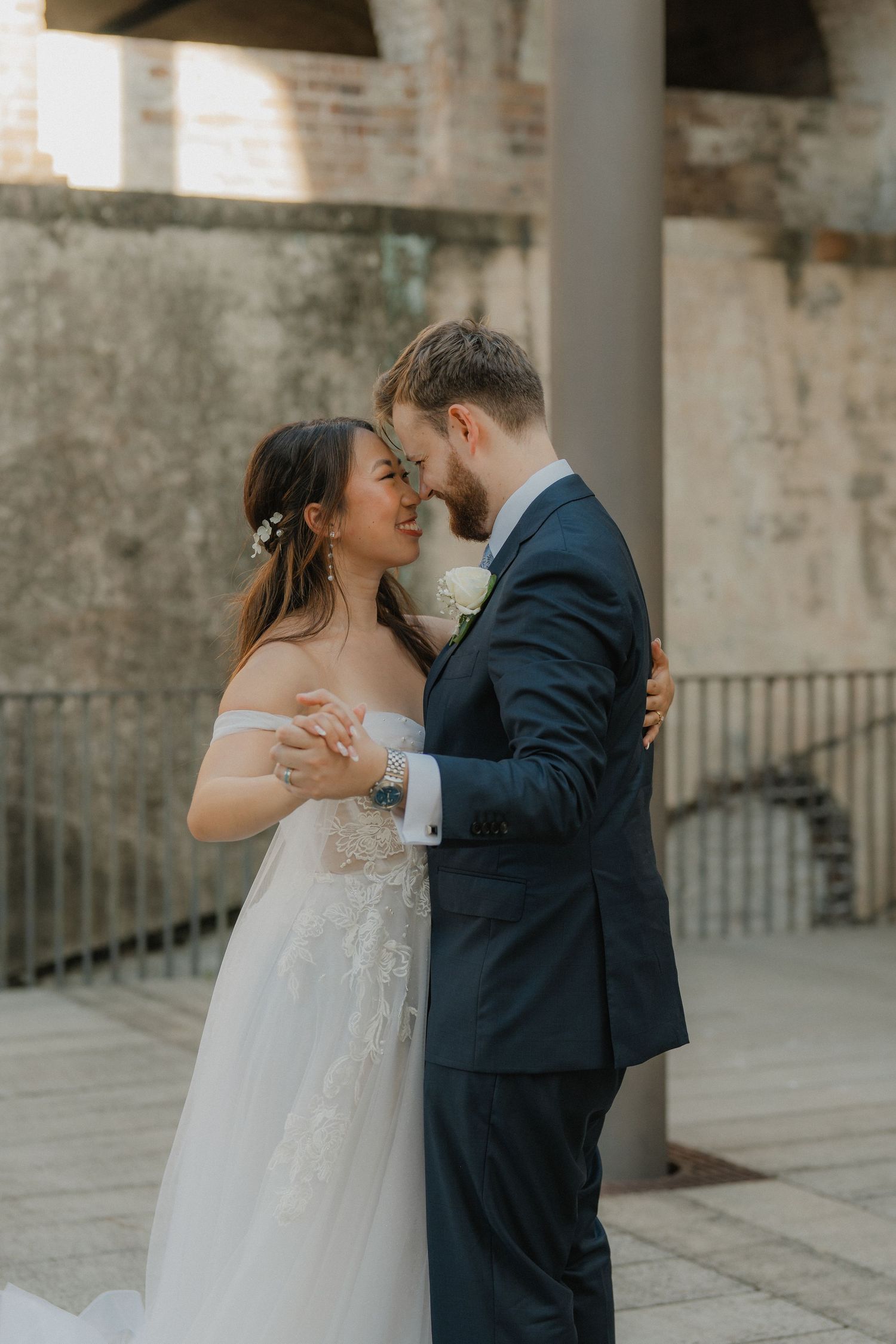 Bride and groom share intimate moments under brick archways during outdoor wedding portraits.