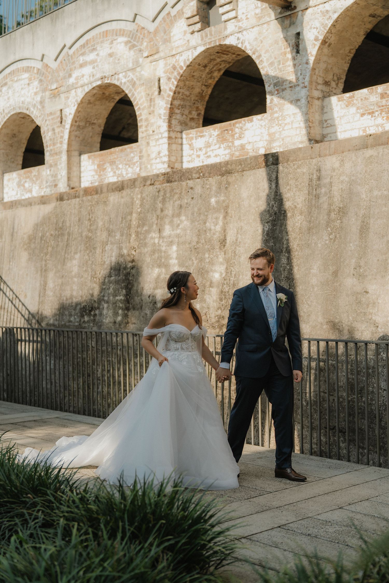 A wedding couple poses together under historic stone archways with dramatic shadows and lighting.