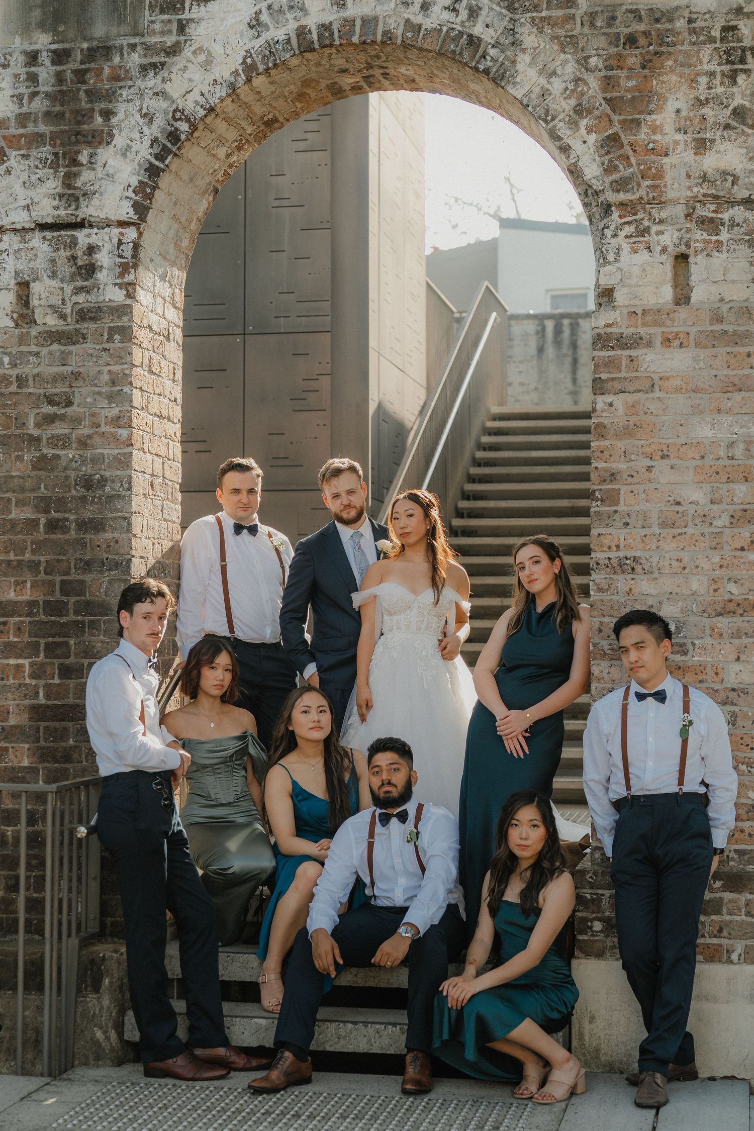 Wedding party poses elegantly on historic brick steps under an arched doorway in formal attire.
