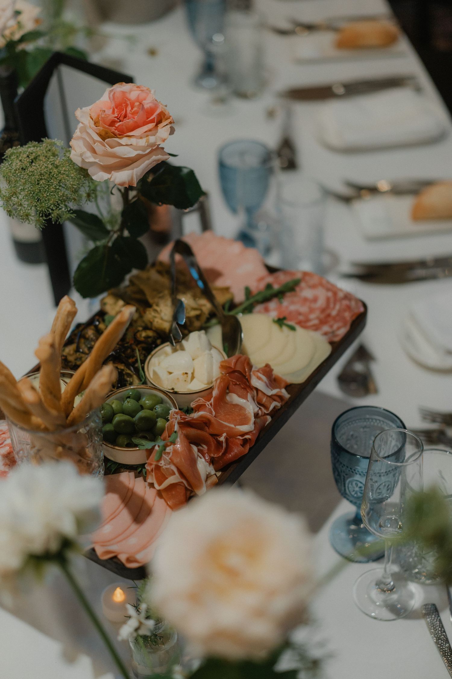 Elegant table setting with blush roses and blue glassware at a wedding reception.
