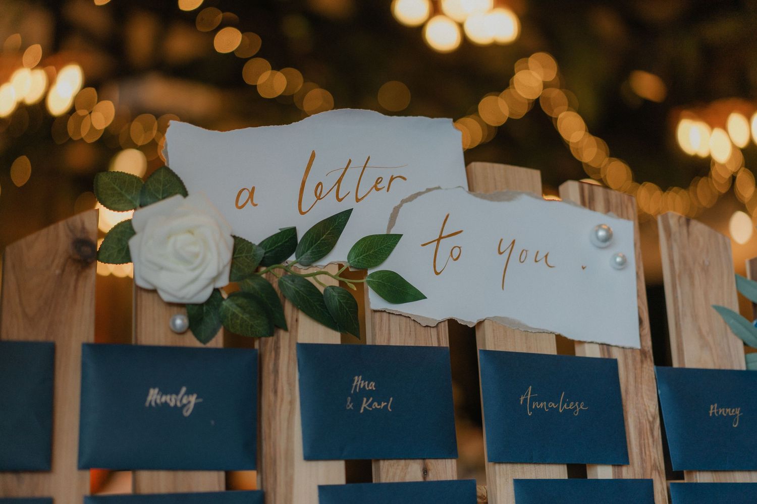 Wedding reception decor featuring blue place cards with elegant calligraphy and twinkle lights in background.
