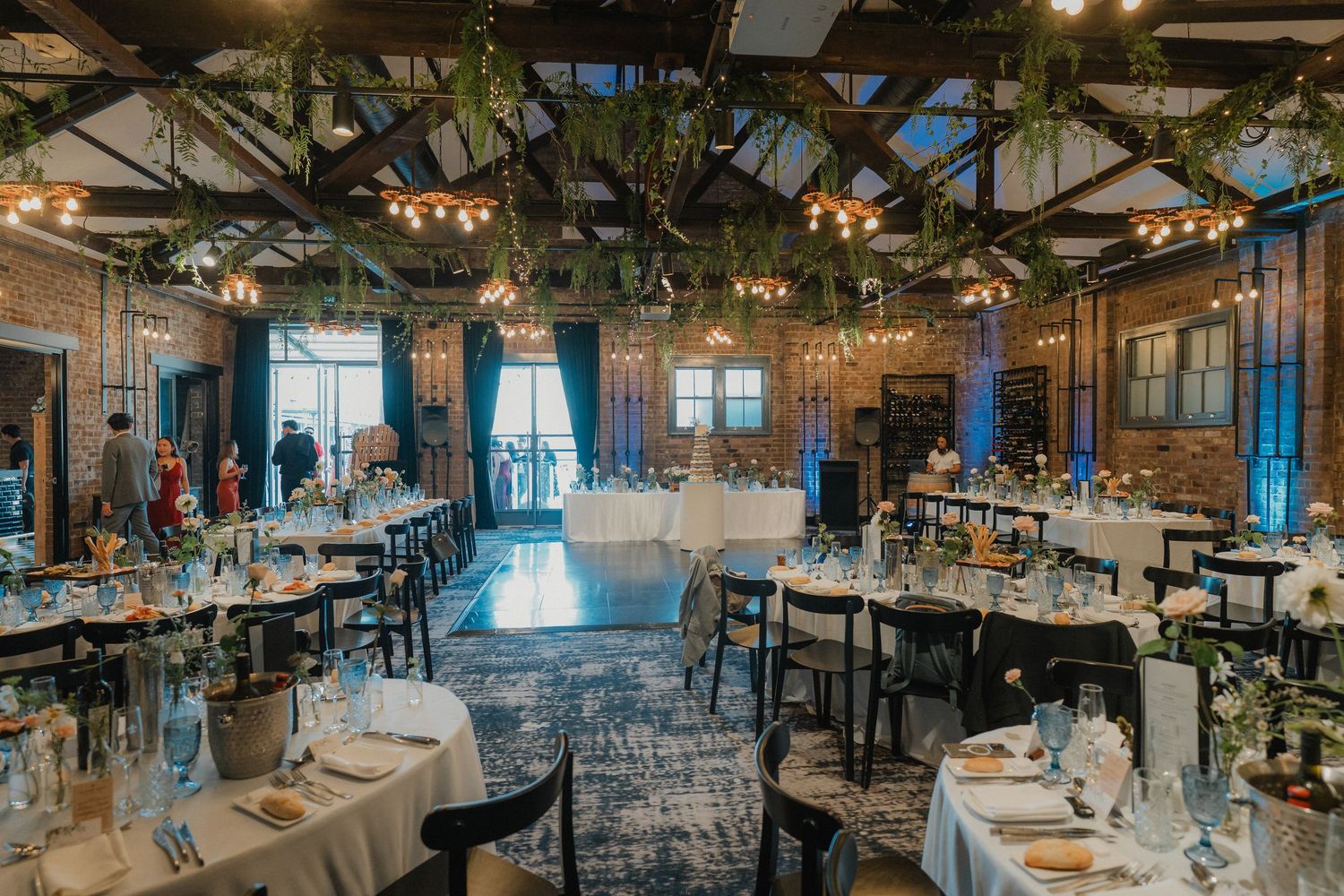 Rustic wedding reception venue with exposed wooden beams, chandeliers, and decorated dinner tables.