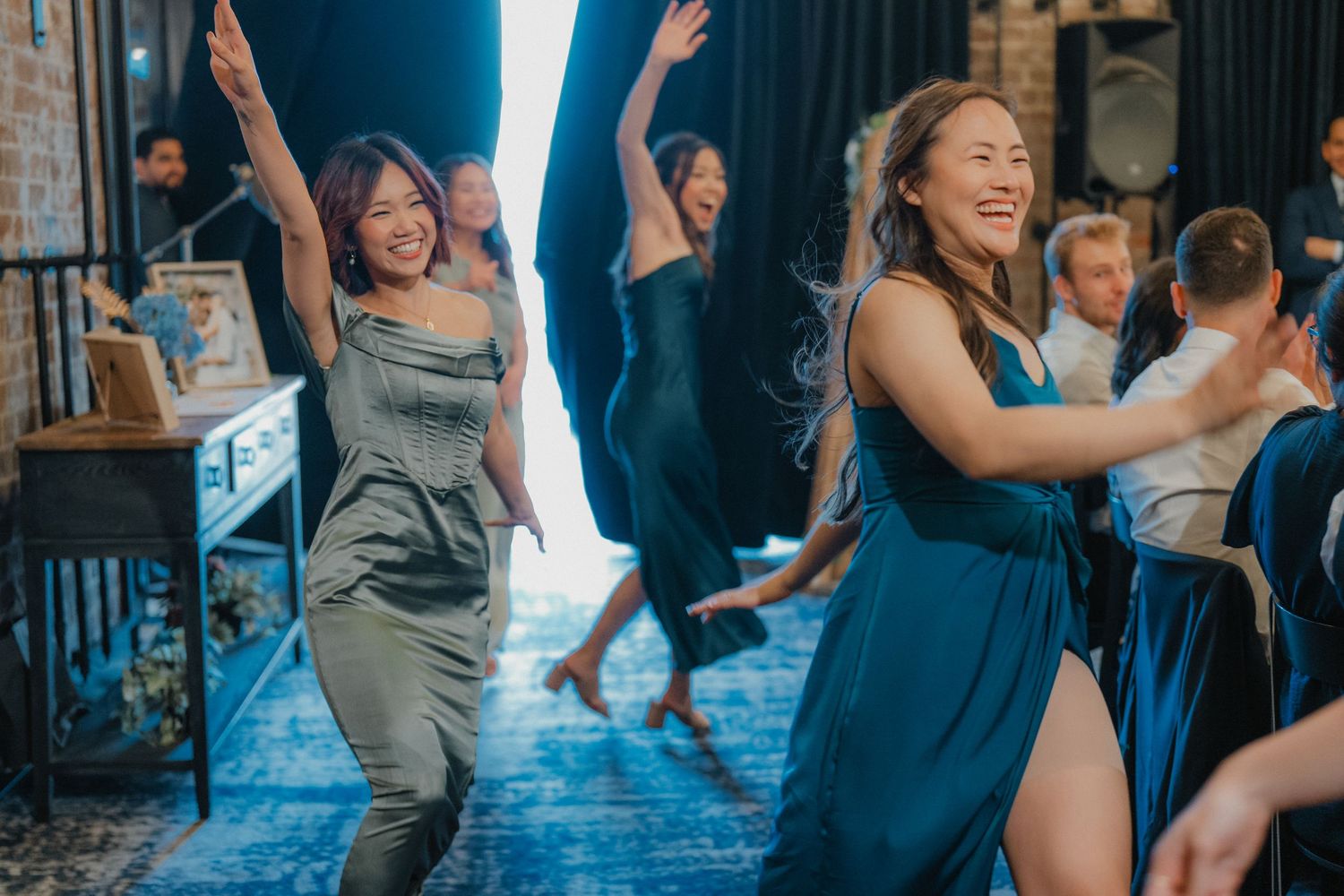 Wedding guests dance and celebrate on a blue-lit dance floor in an industrial-chic venue.