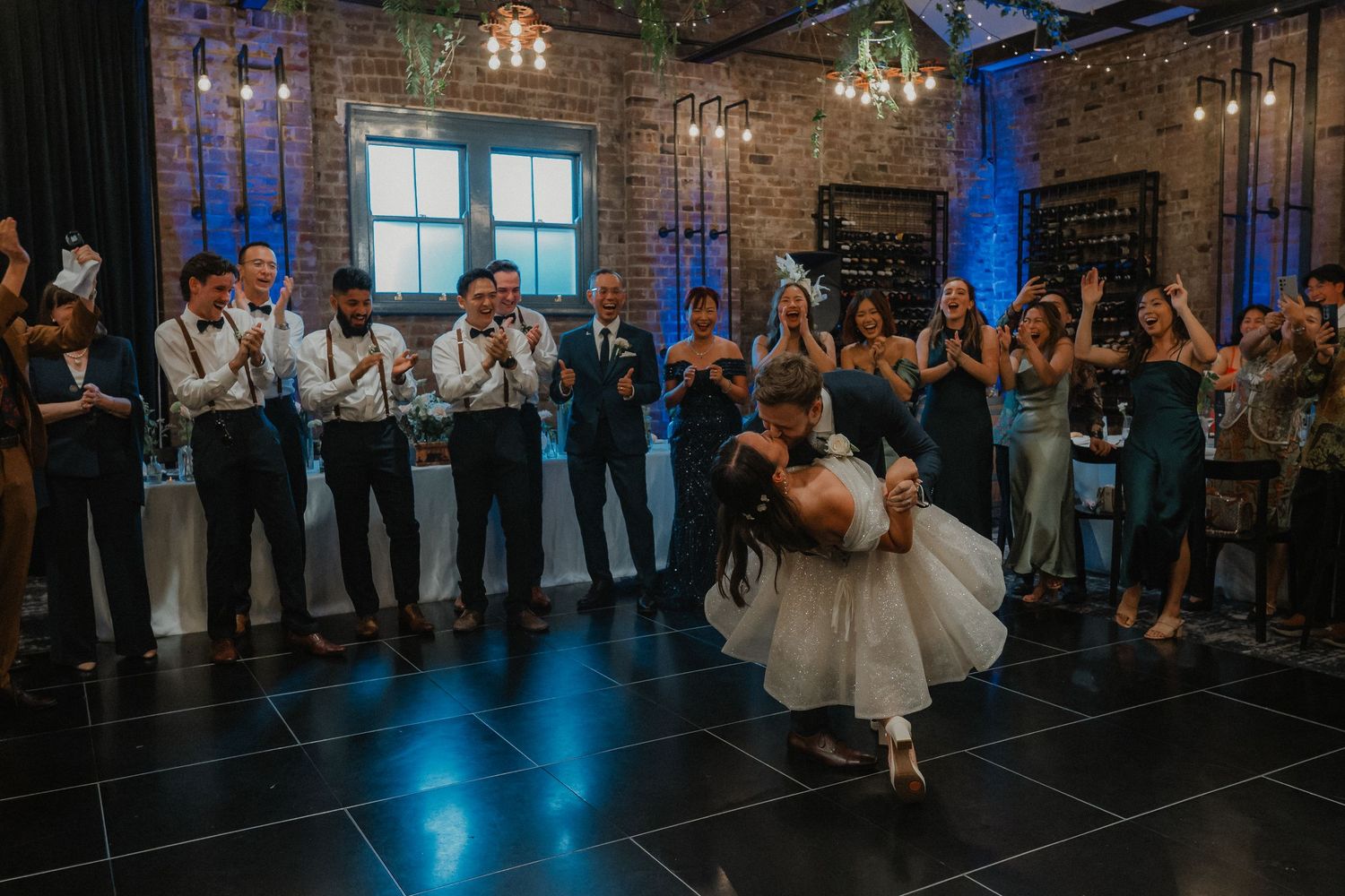 A couple performs a dip during their wedding dance as guests cheer.