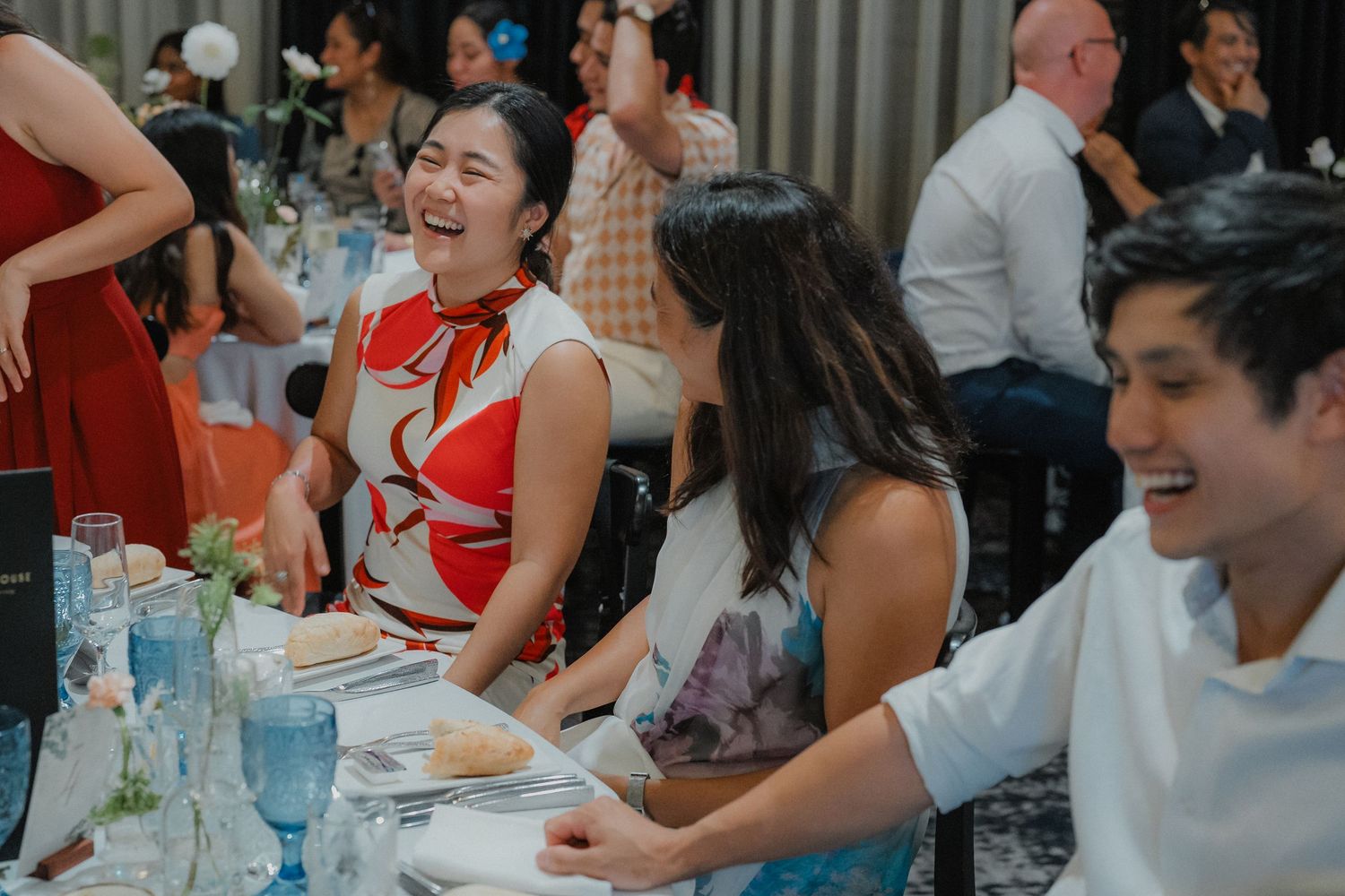 Wedding reception guests enjoying dinner and conversation at tables decorated with blue glassware.