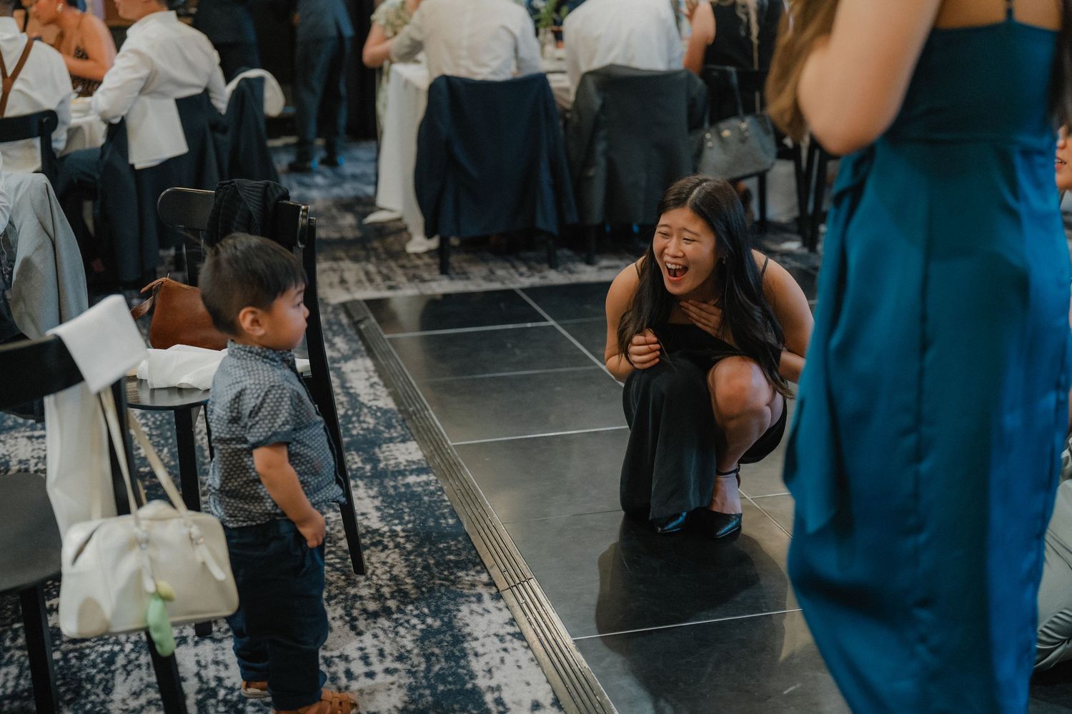 Wedding guests dance and interact on a patterned dance floor at an indoor reception.