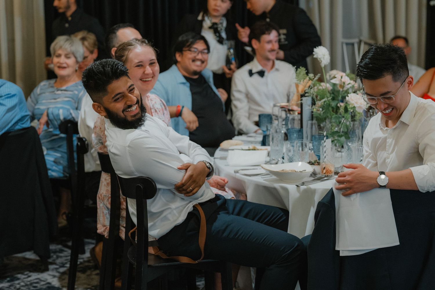 Wedding reception guests sharing joyful moments around decorated dining tables.