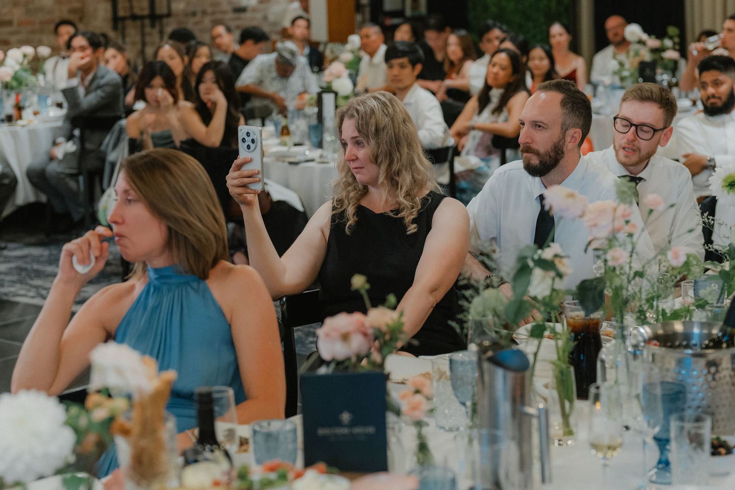 Wedding guests seated at decorated reception tables with floral centerpieces.