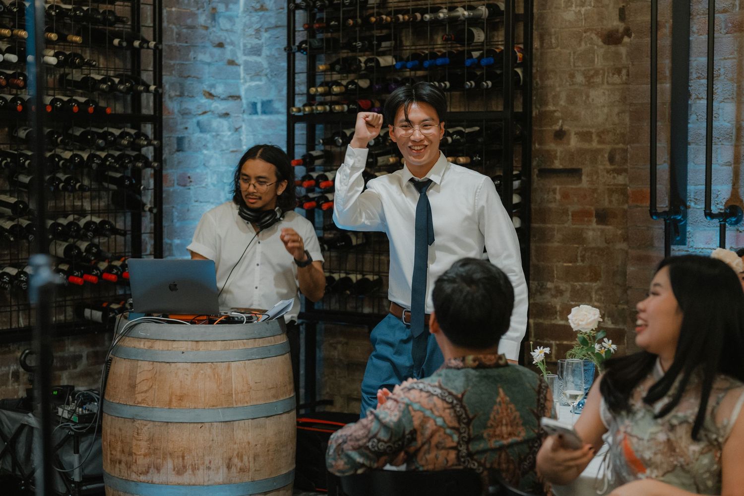 Wedding guests enjoying a reception celebration at a rustic venue with wine barrels.