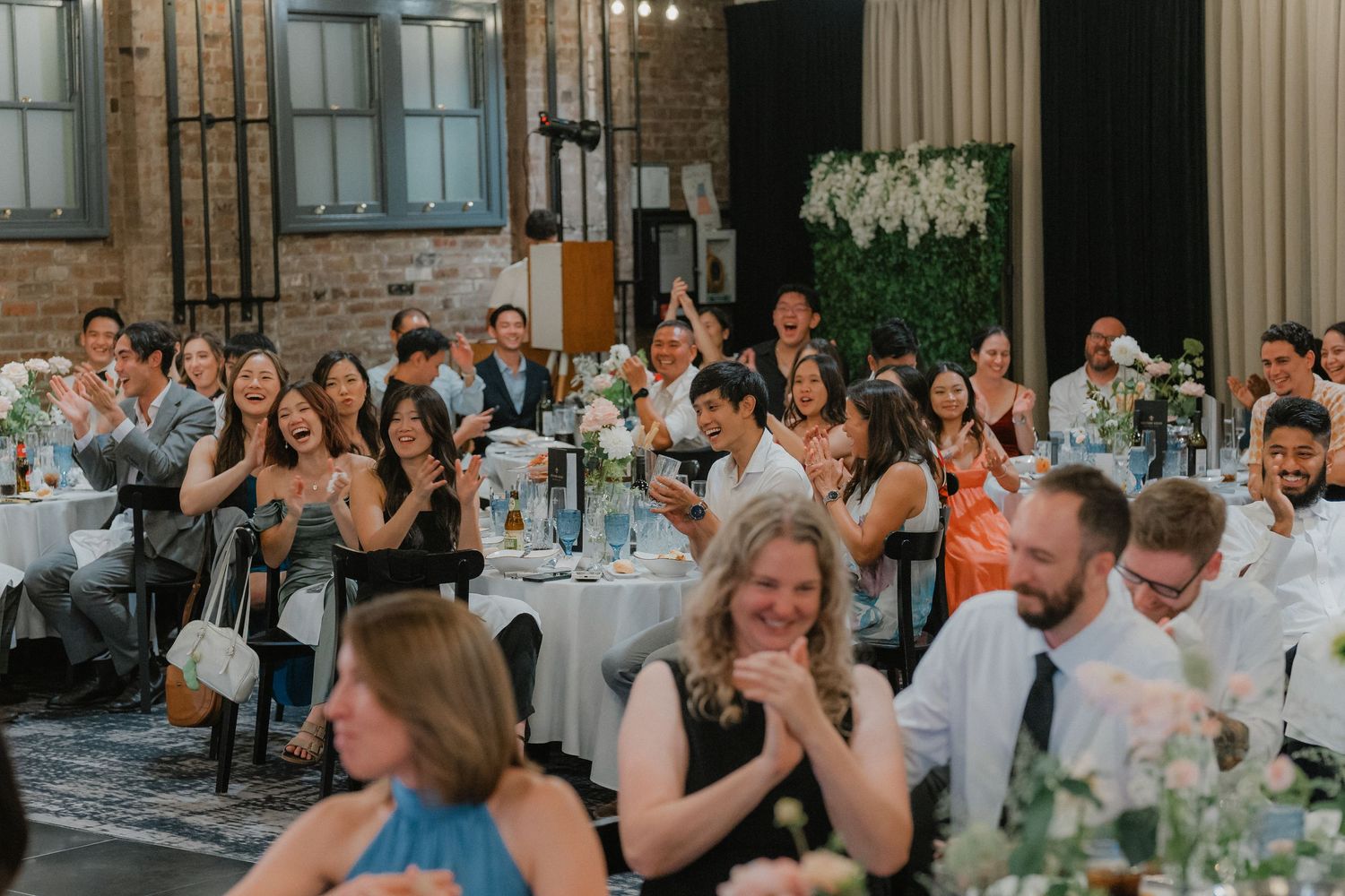 Wedding reception celebration showing guests seated at decorated tables in an industrial-style venue.