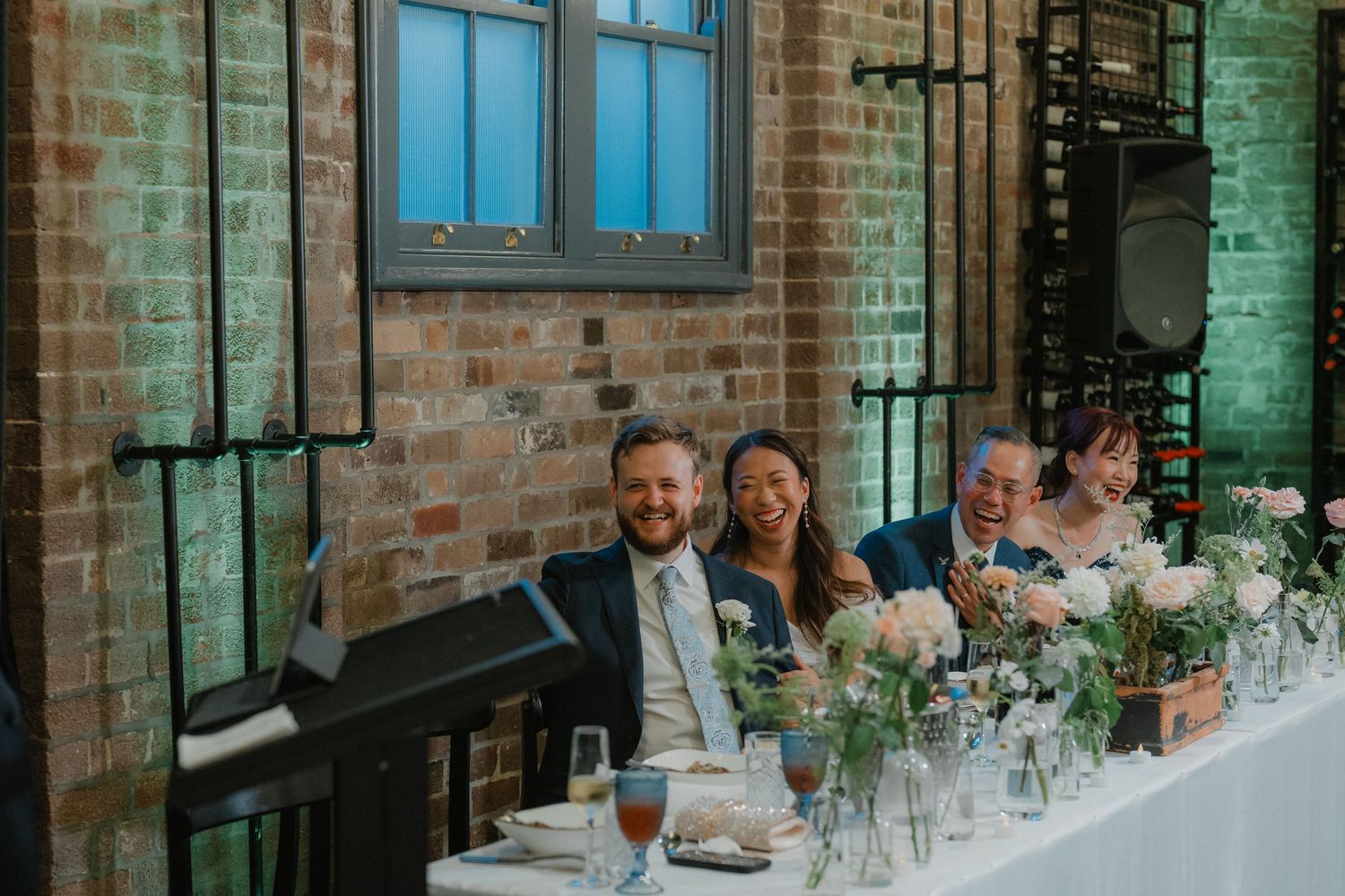 Long dining tables set up for a wedding reception in an industrial venue with brick walls and large windows.