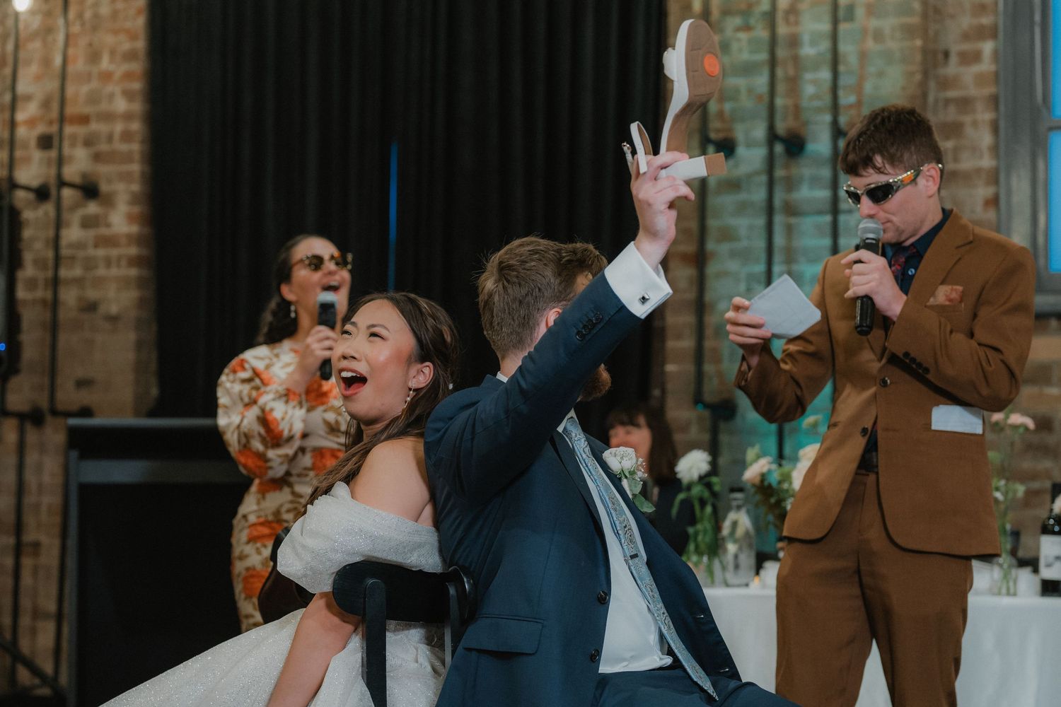 Wedding guests celebrate during reception festivities in an industrial brick venue space.