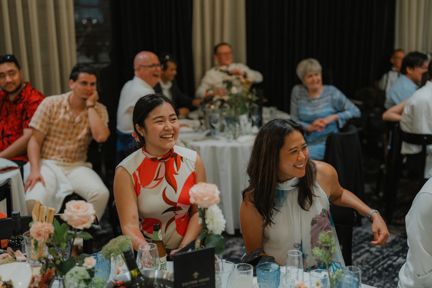 Party guests laugh and enjoy themselves at an elegant dinner reception with floral centerpieces and table settings.