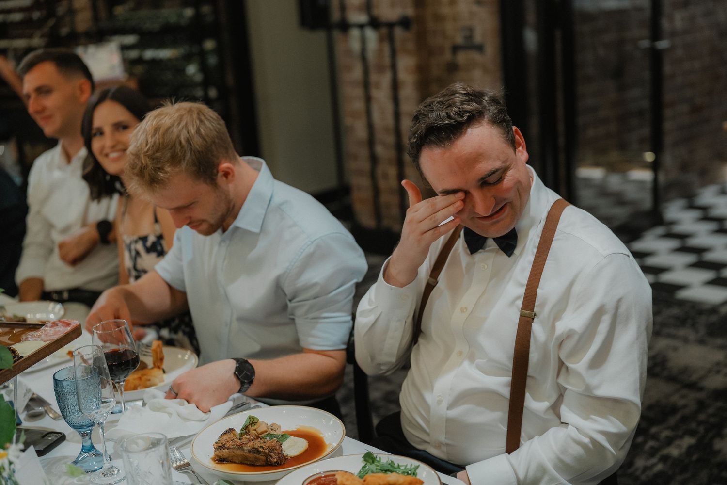 Wedding reception dinner service in a rustic venue with exposed brick walls.