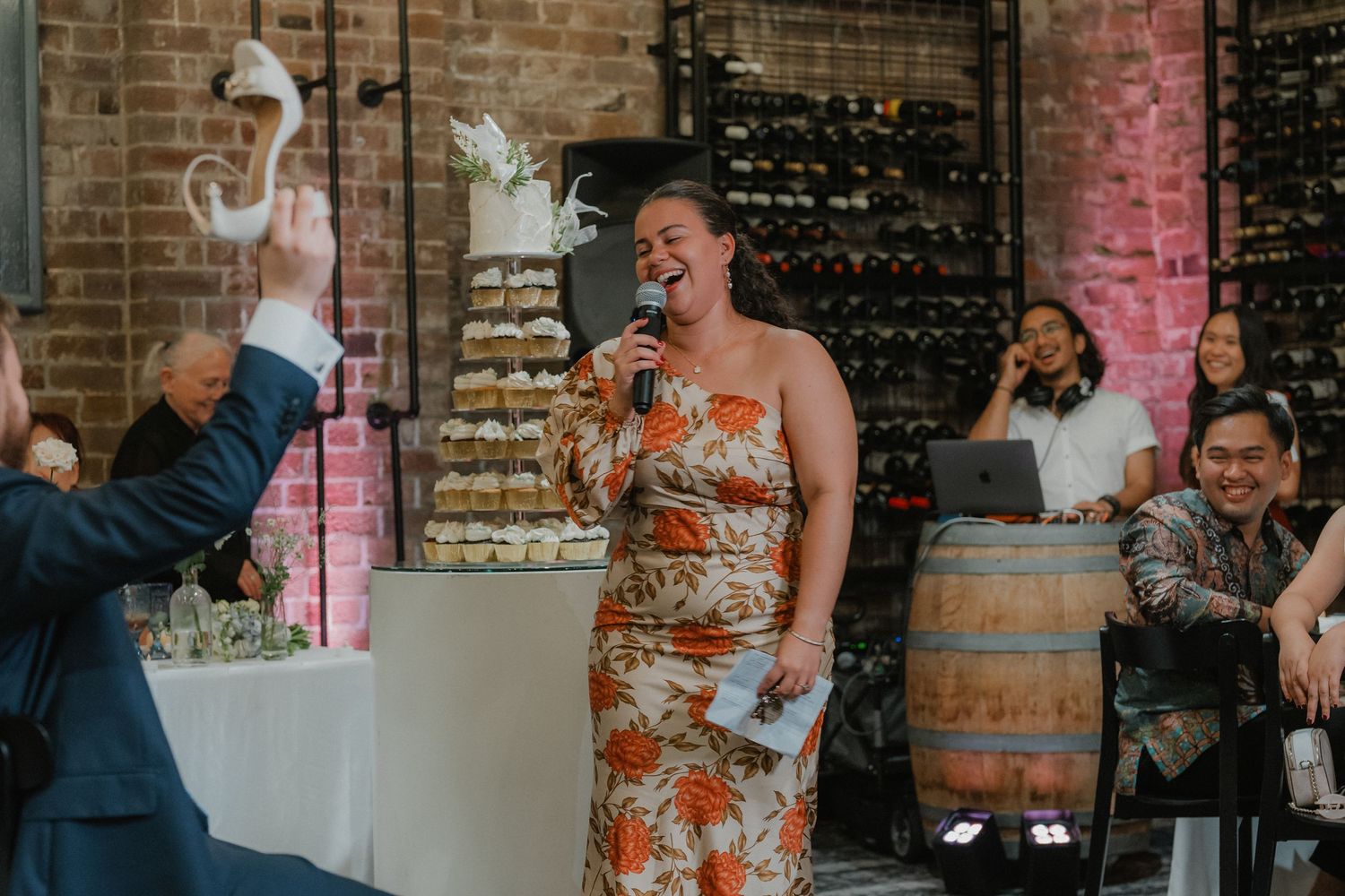 Guests dancing and laughing at a wedding reception in a rustic brick venue with colorful lighting.