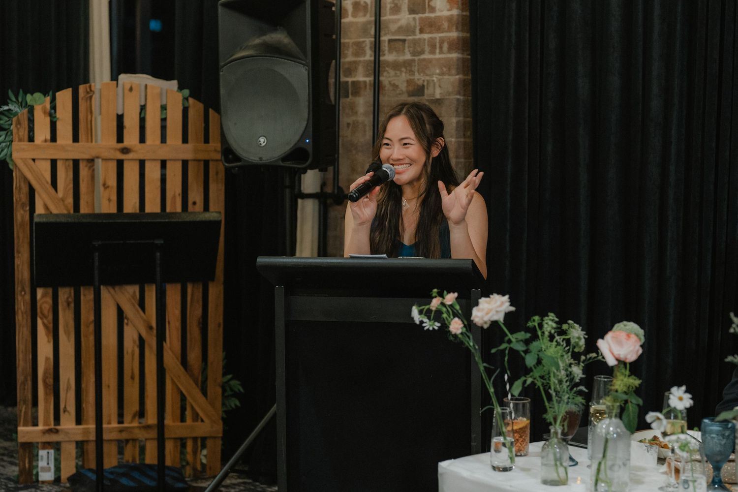 A person speaks at a podium with white flowers and greenery displayed on a side table.
