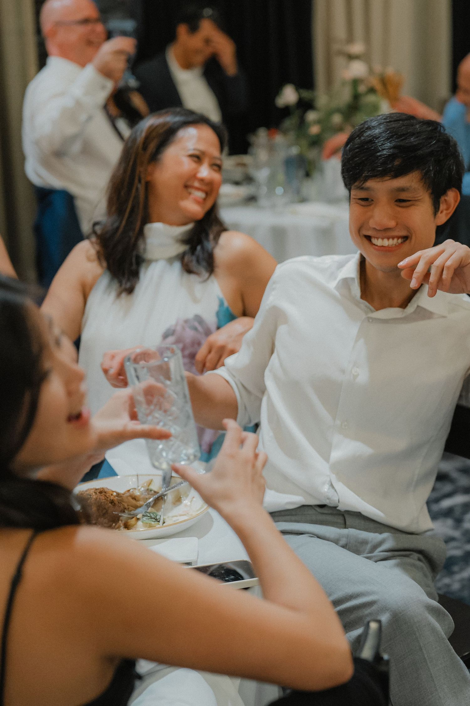 Wedding guests share joyful conversation around a dinner table at an indoor reception.