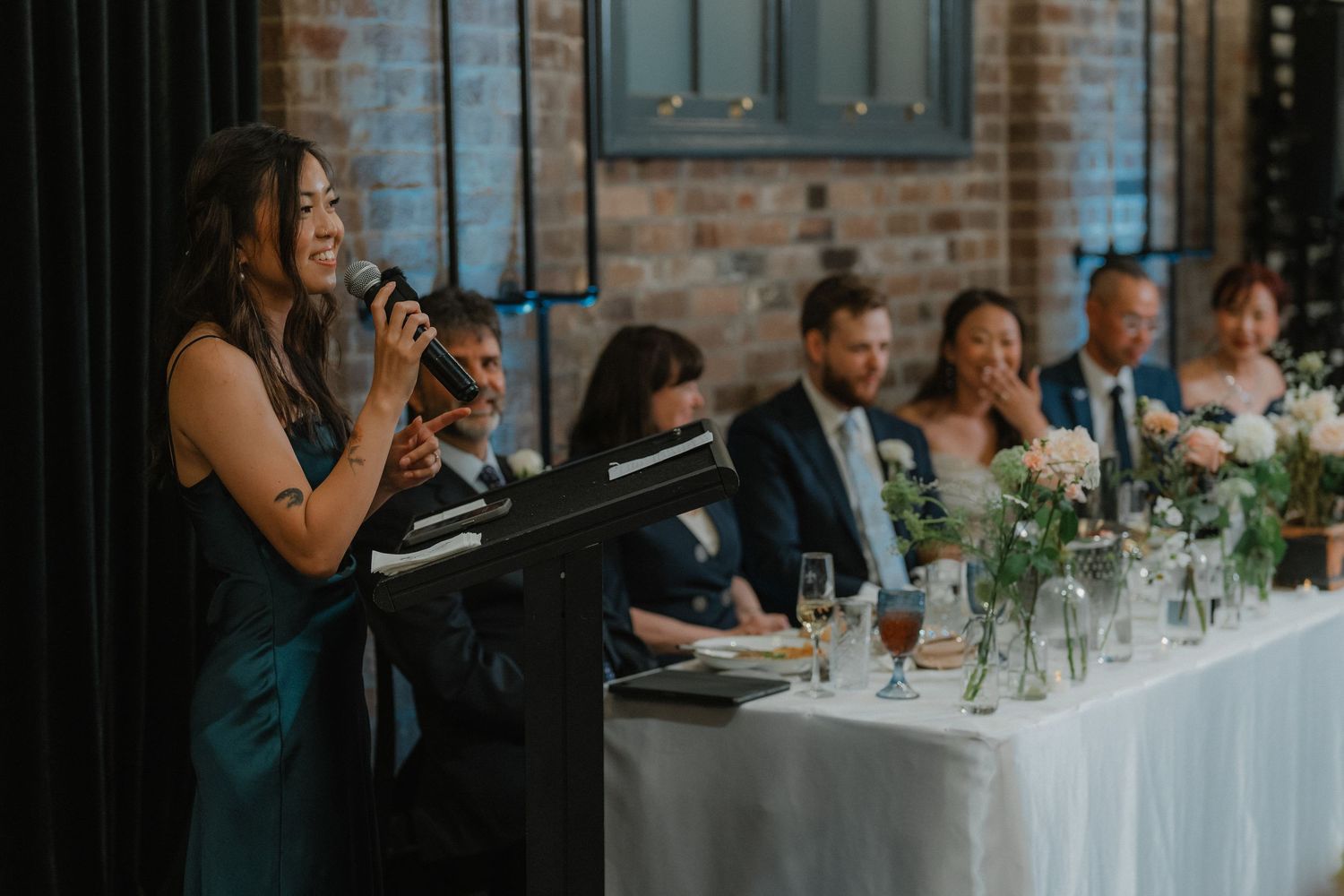 Wedding reception tables with elegant white linens and floral centerpieces against exposed brick walls.
