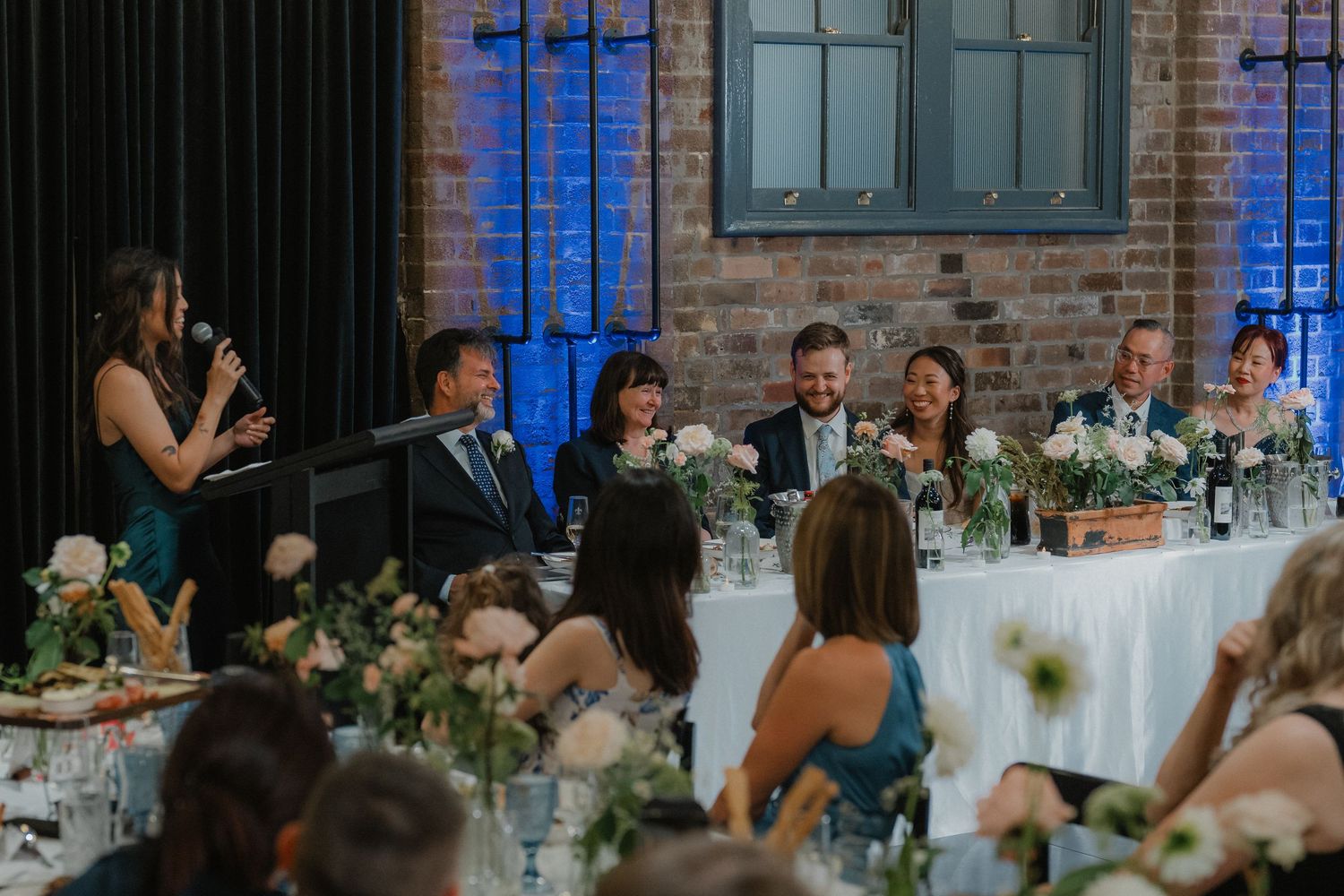 Wedding reception setup featuring elegant table settings in a historic venue with exposed brick walls and blue lighting.