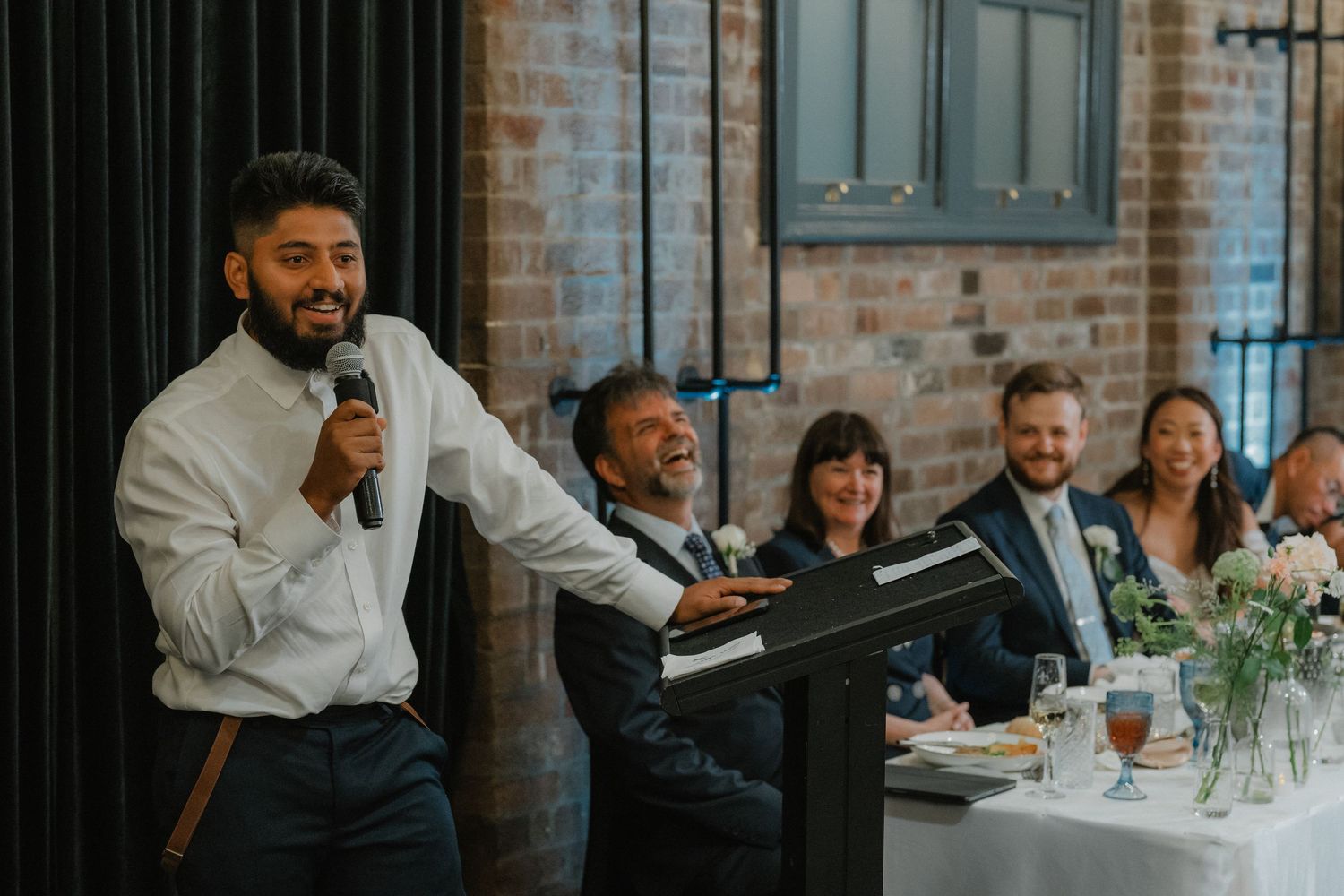 Wedding reception guests seated at dining tables in an industrial brick venue.