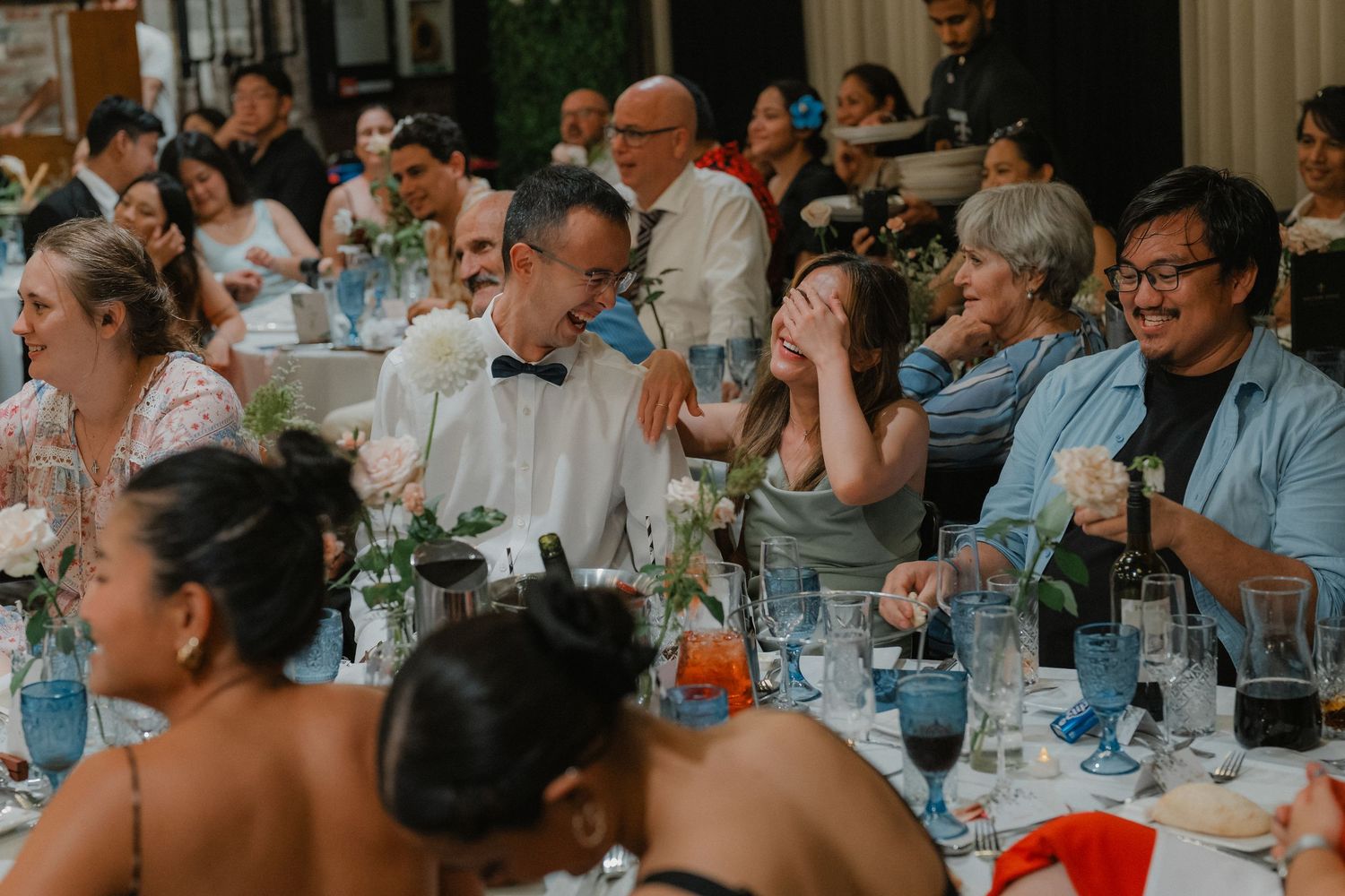 Wedding reception dining setup with guests seated at long tables in an industrial-chic venue.