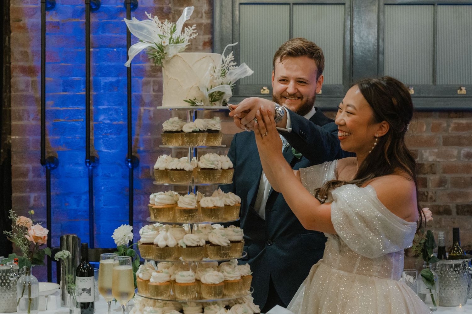 Wedding couple poses next to a tiered cupcake display with blue uplighting in the background.